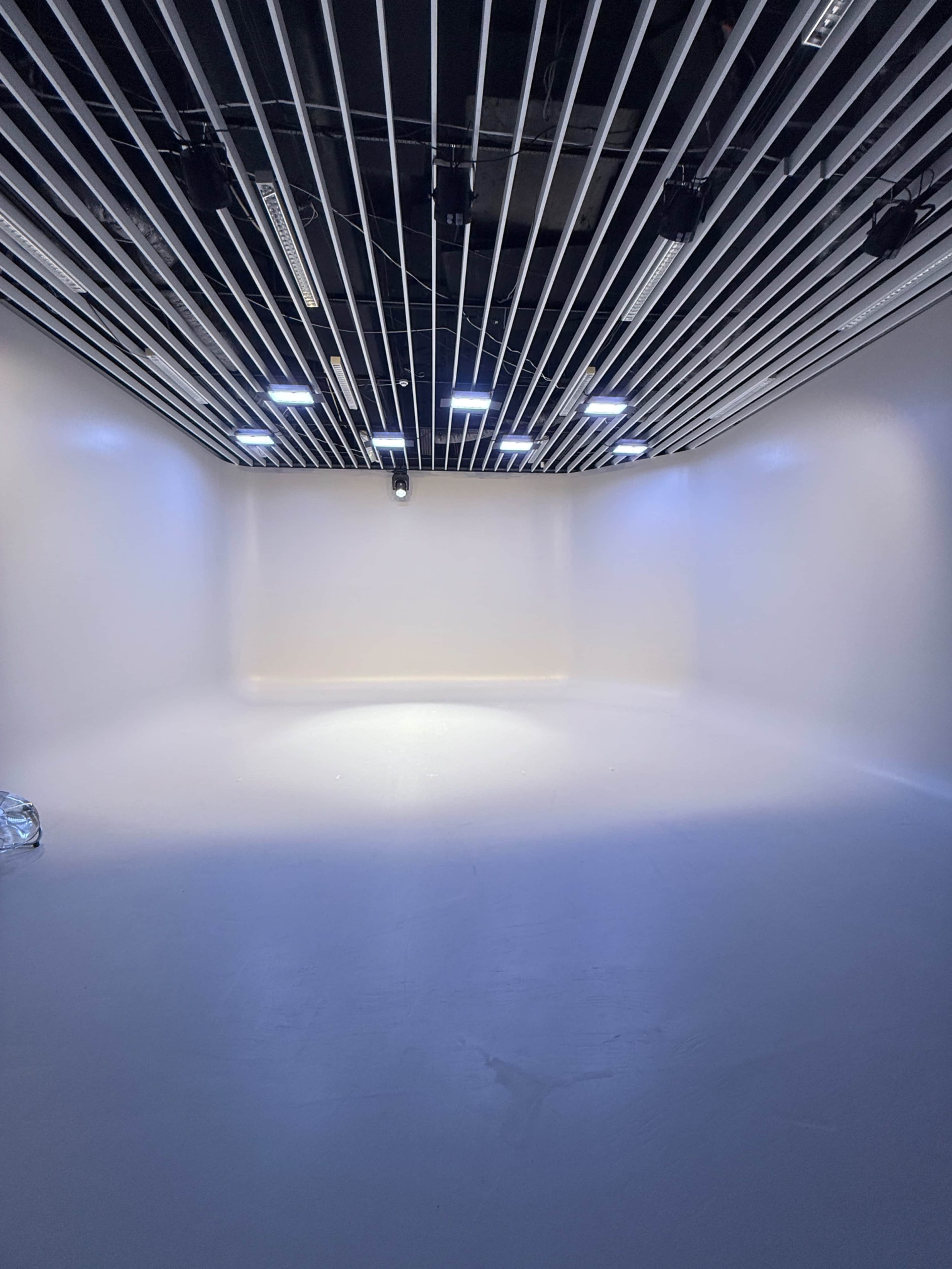 The image shows a stark white studio space with overhead lighting and a smooth floor.