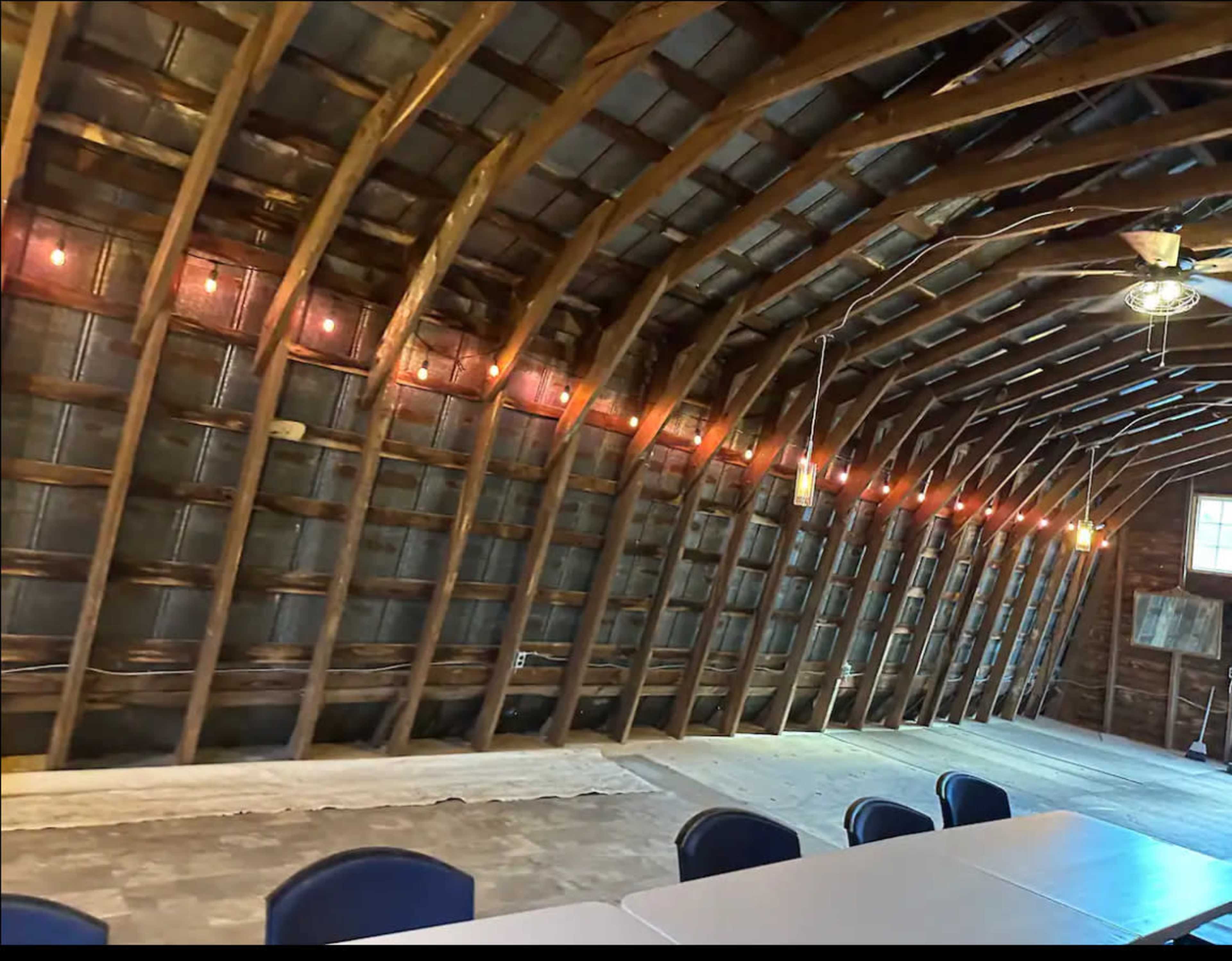 The interior of a wooden barn with exposed beams and a long table set up along the center.