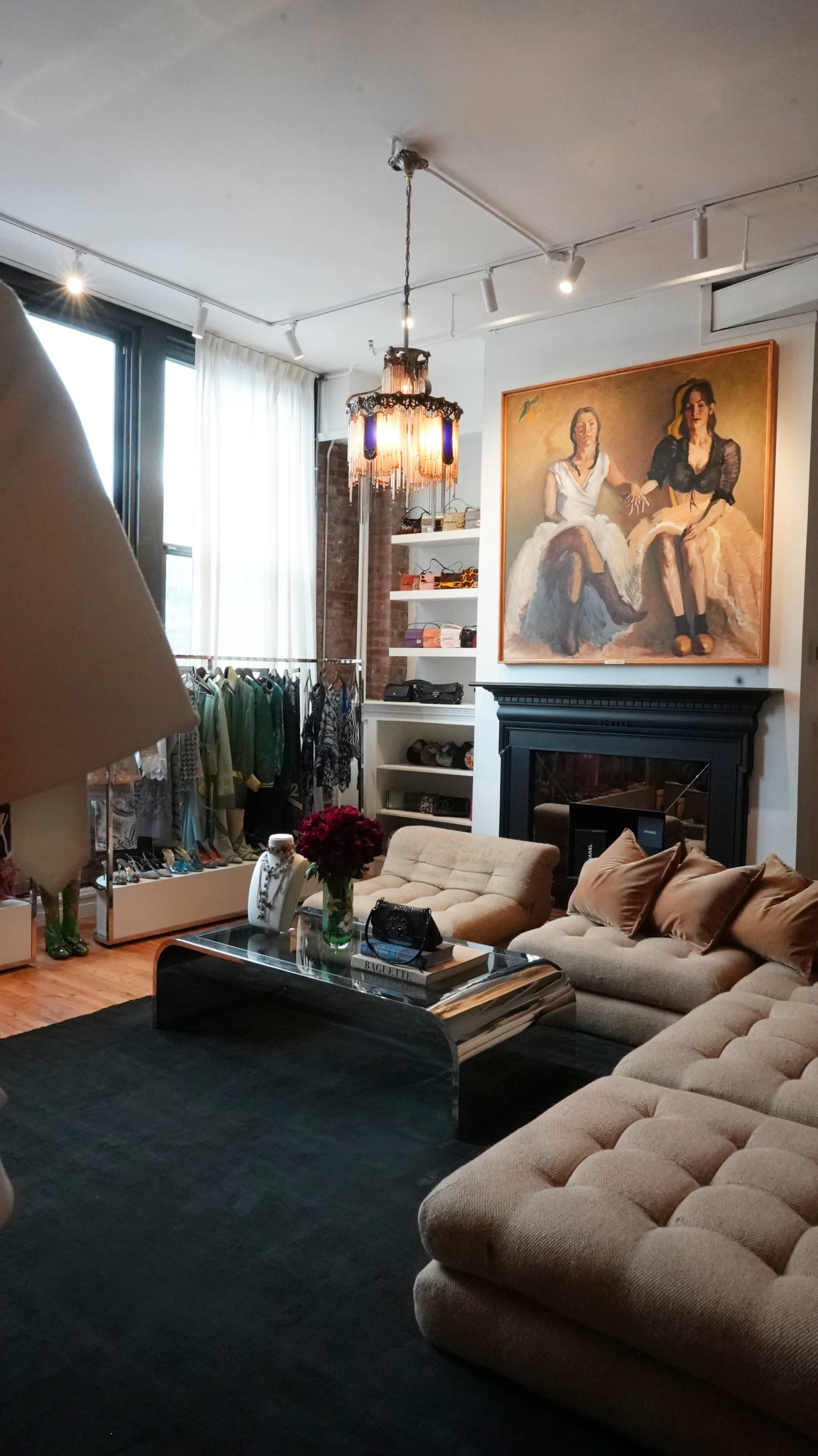 The image shows a stylish boutique with a cozy seating area, a large painting on the wall, clothing racks in the background, and a coffee table at the center.