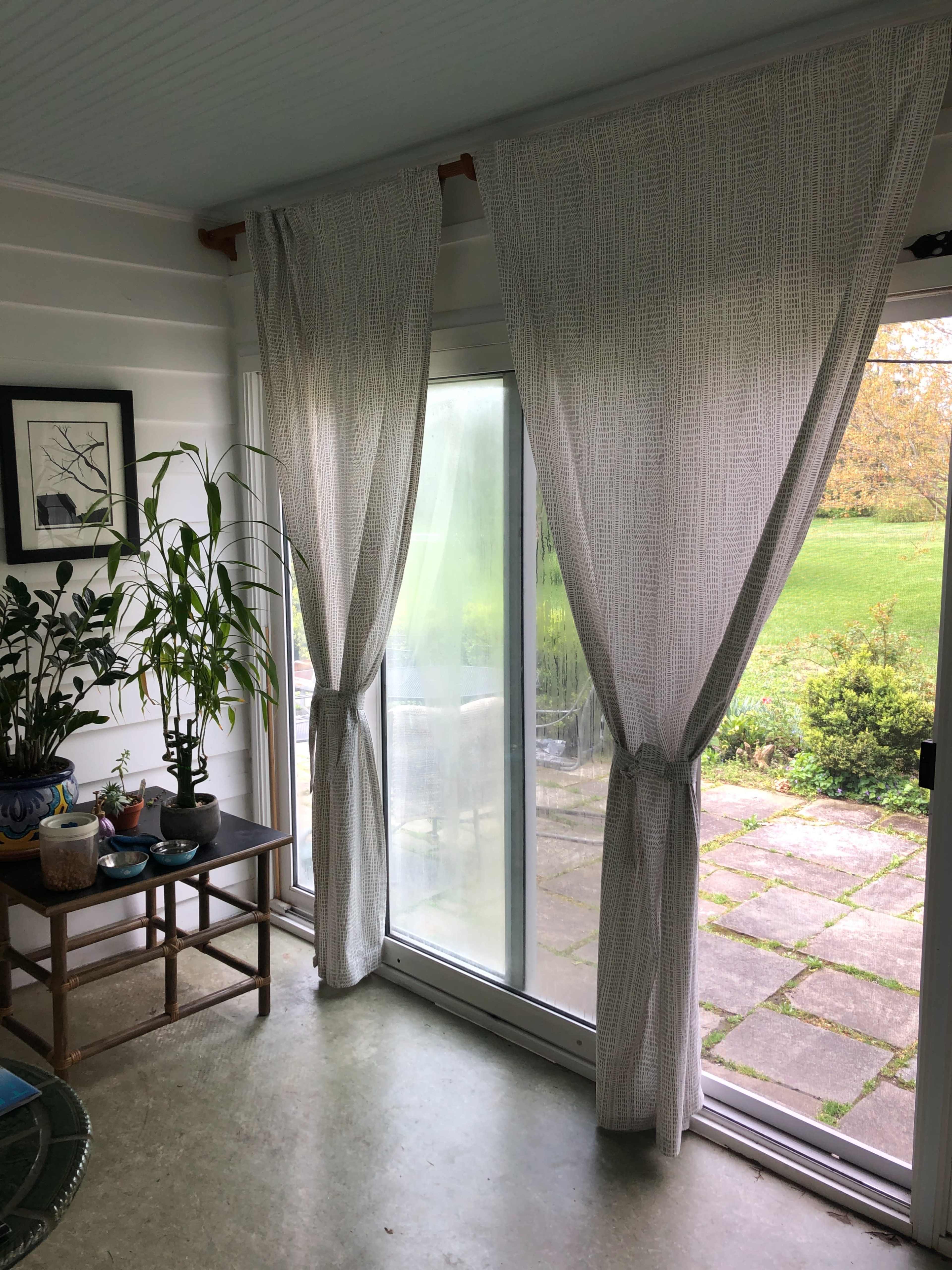 A sunlit room features two curtains framing a large glass door that opens to a grassy outdoor area.