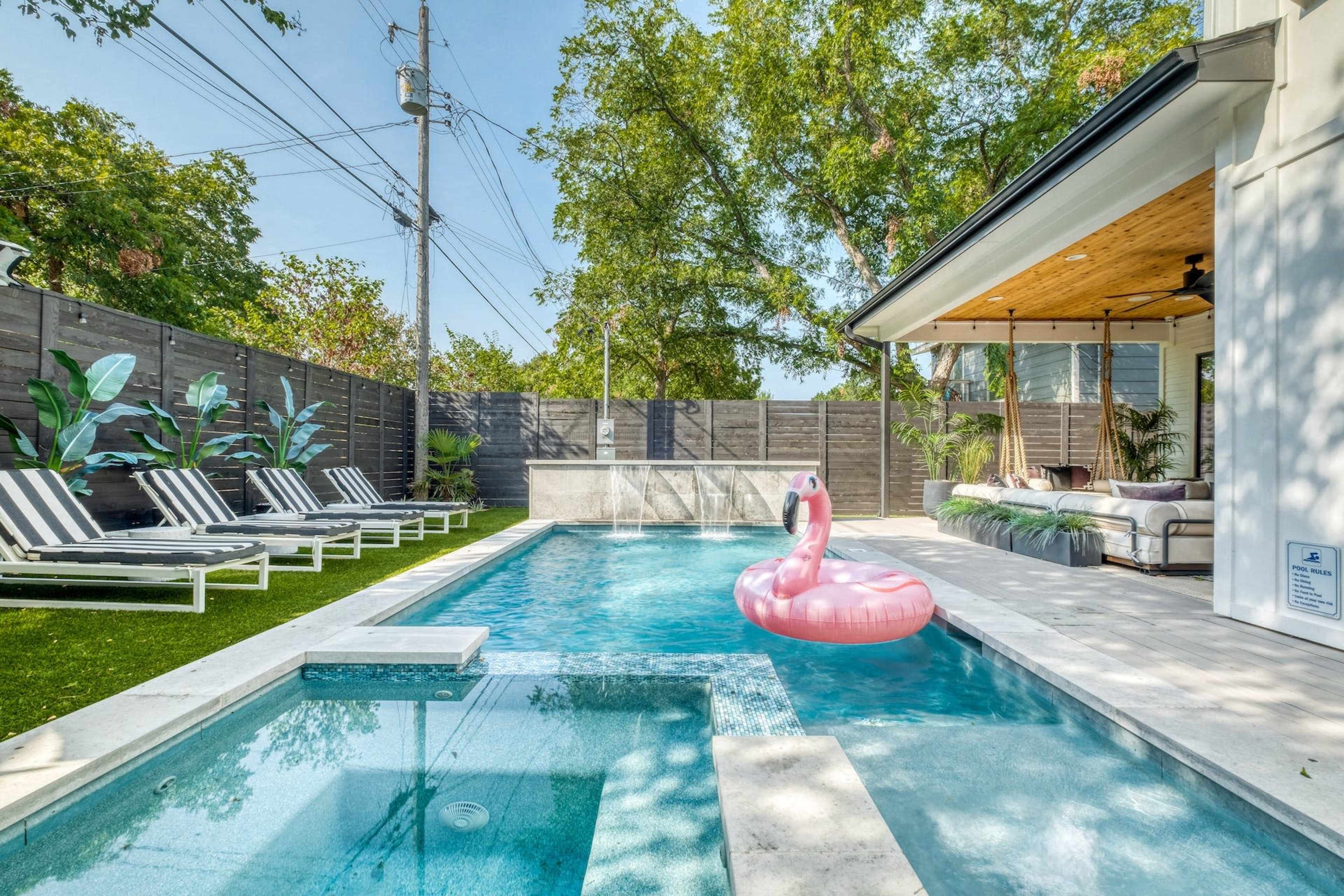 A pink flamingo float sits in a blue swimming pool surrounded by lounge chairs and landscaped greenery.
