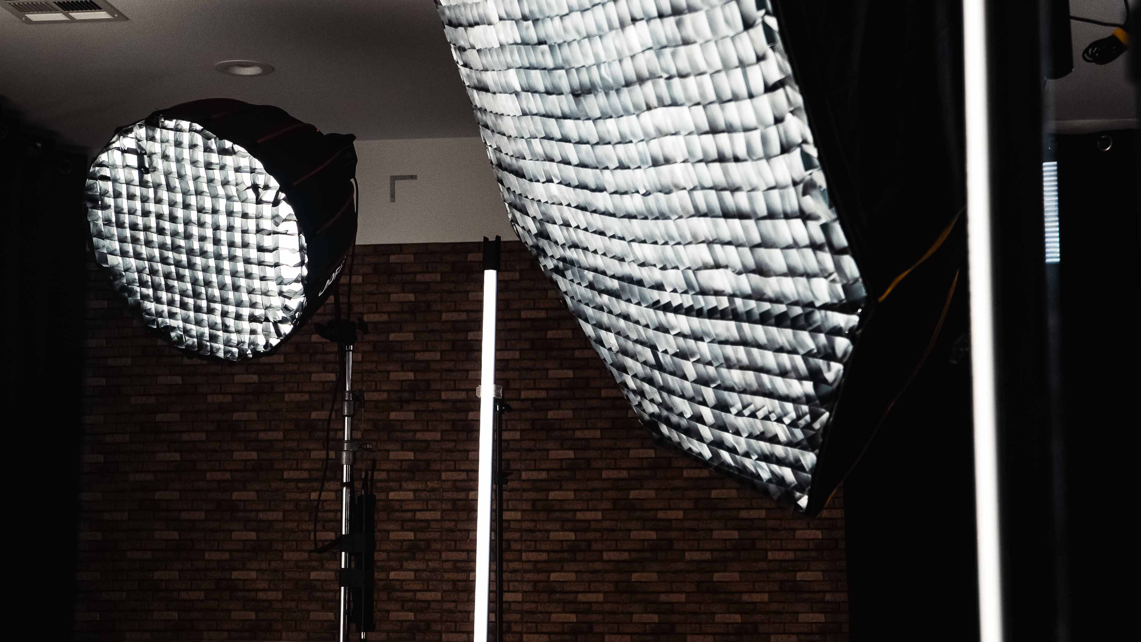 The image shows two large studio lights mounted on stands, with a textured brick wall in the background.