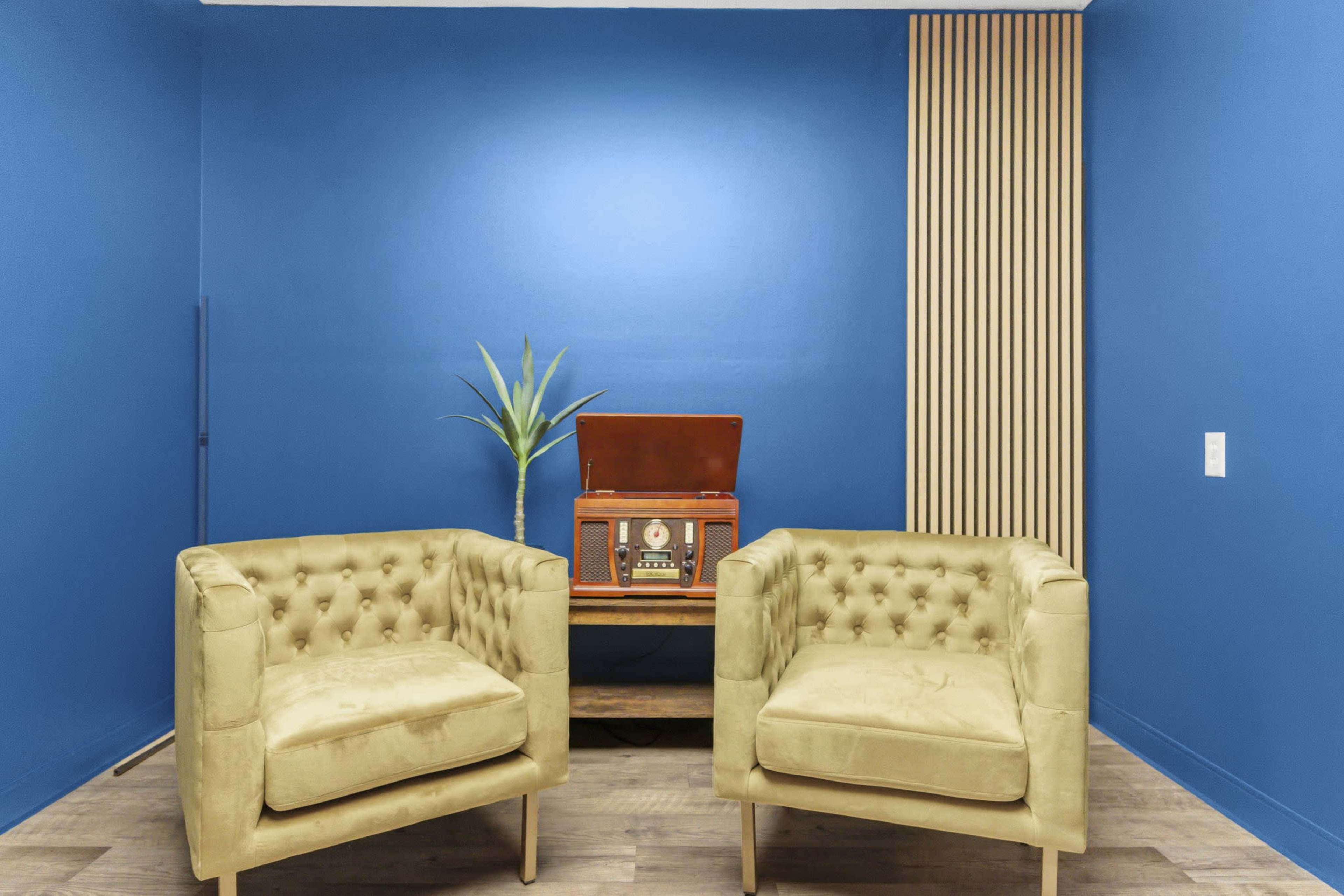The image shows two tufted yellow chairs facing a vintage record player against a blue wall with wooden paneling.