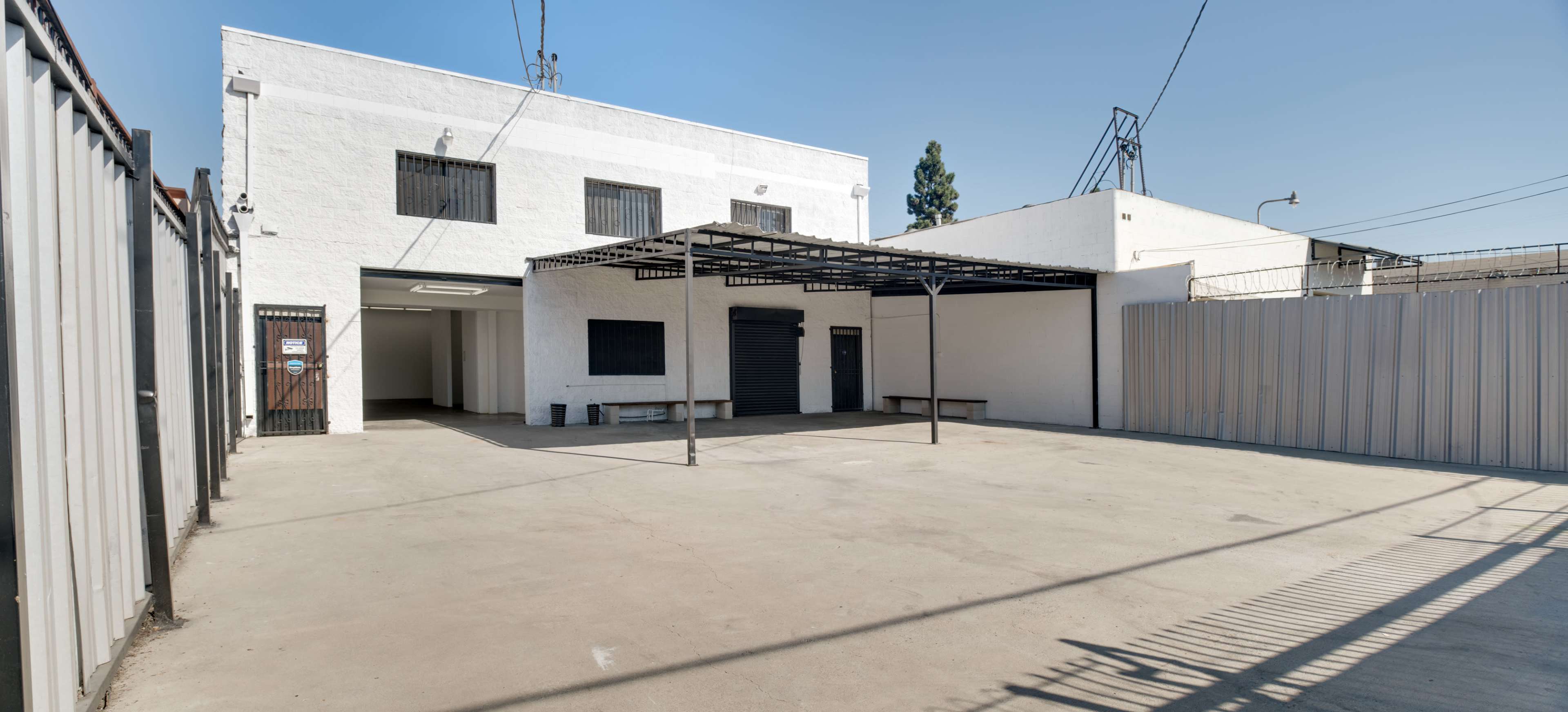 A large, empty concrete courtyard surrounded by walls and buildings with a covered area supported by metal poles.