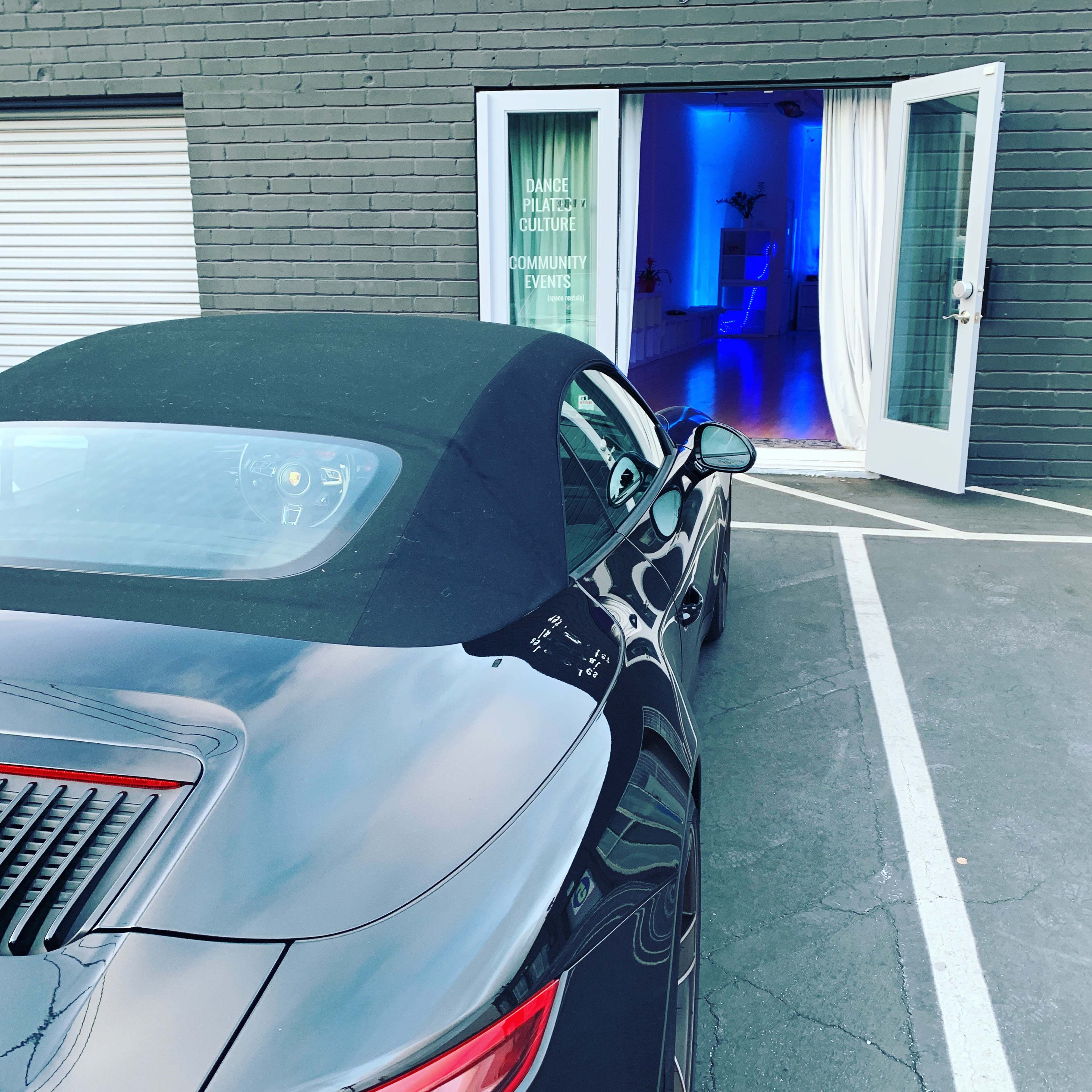 A black convertible sports car is parked in front of a building with an open door illuminated by blue lights.