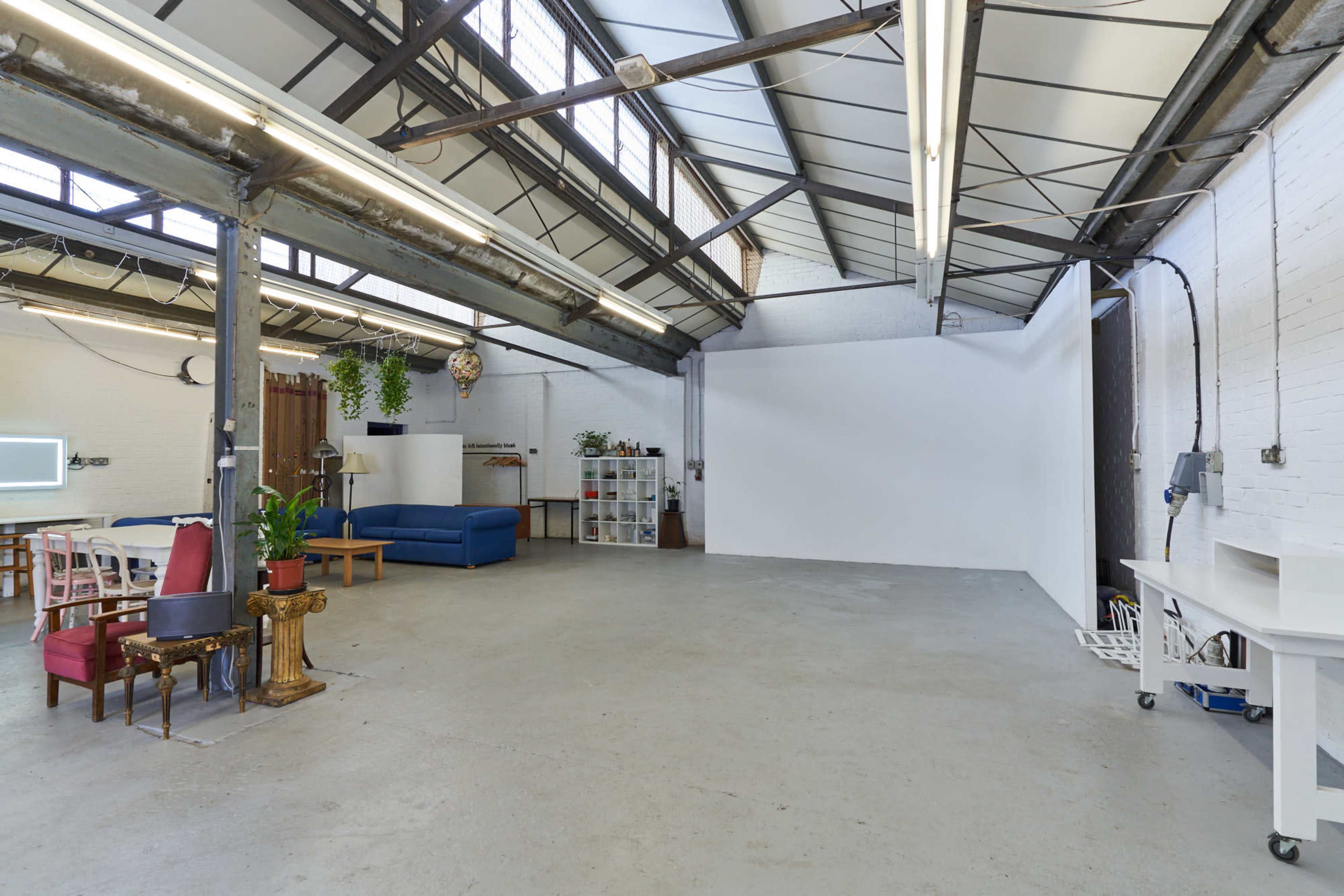 A spacious industrial-style room with high ceilings, a white wall, various seating areas, and shelves.