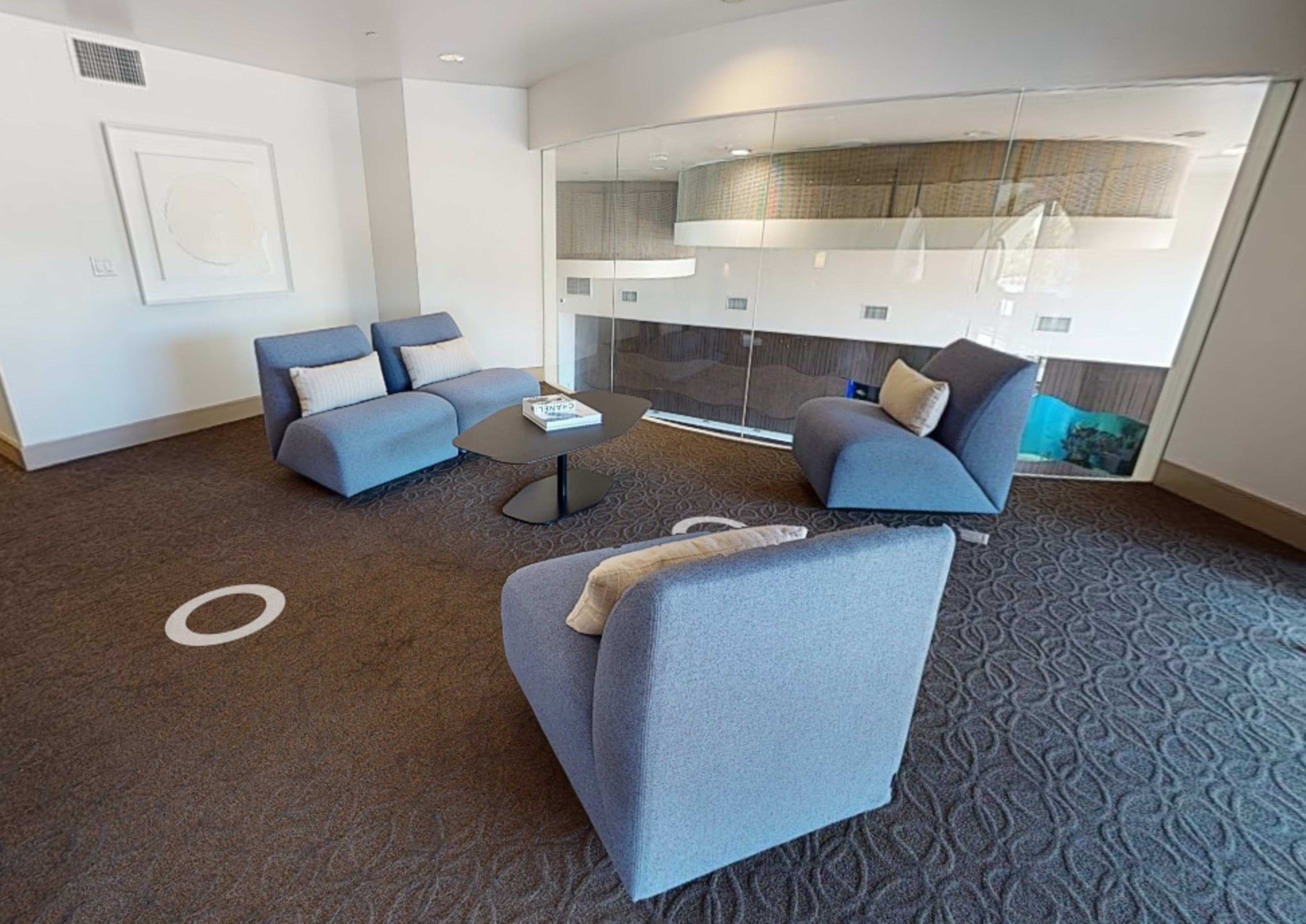 A modern lounge area with two gray armchairs and a small black coffee table in a well-lit space featuring glass walls.