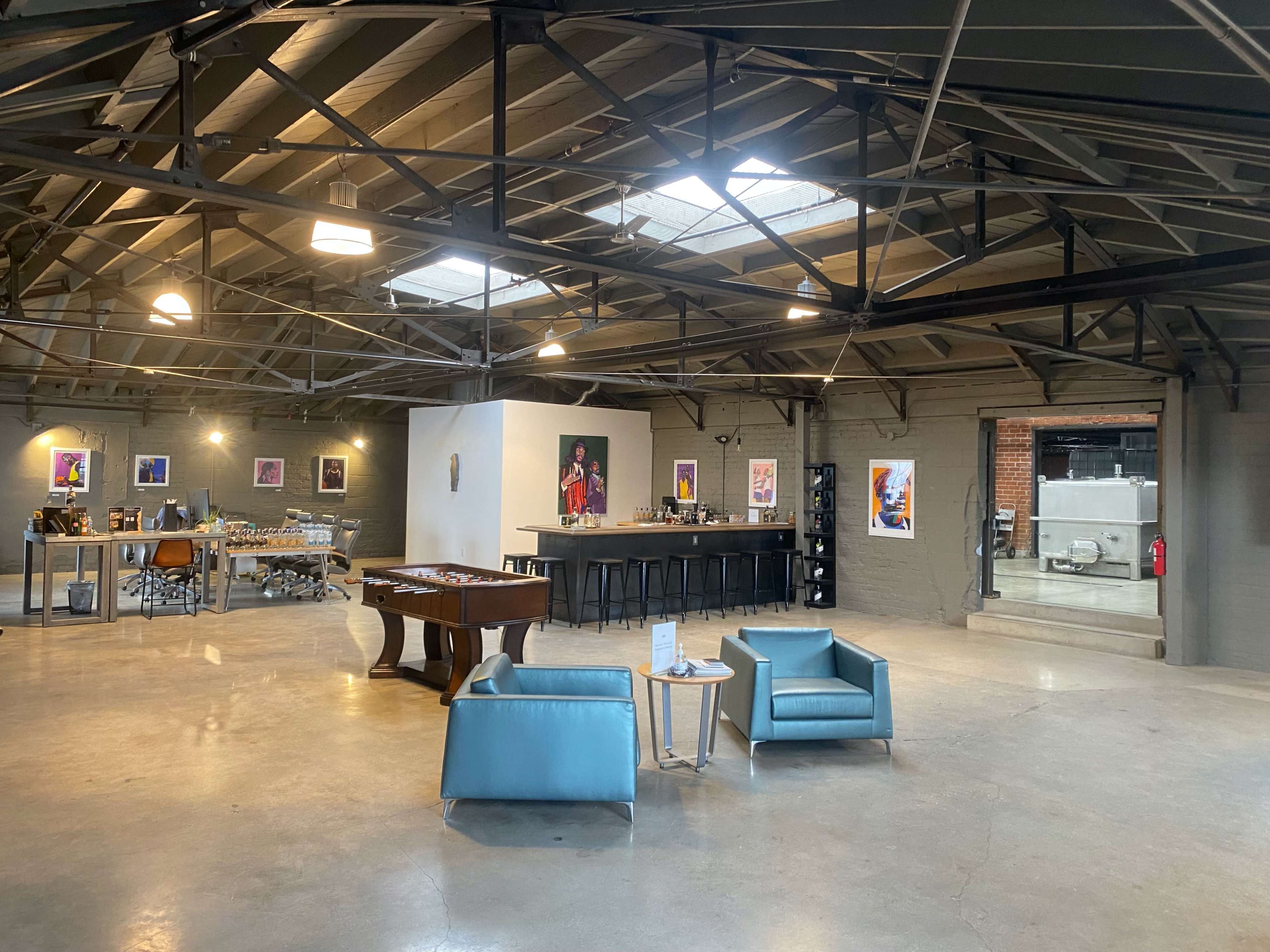 A spacious industrial-style room with a bar area, a pool table, two chairs, and artwork displayed on the walls.