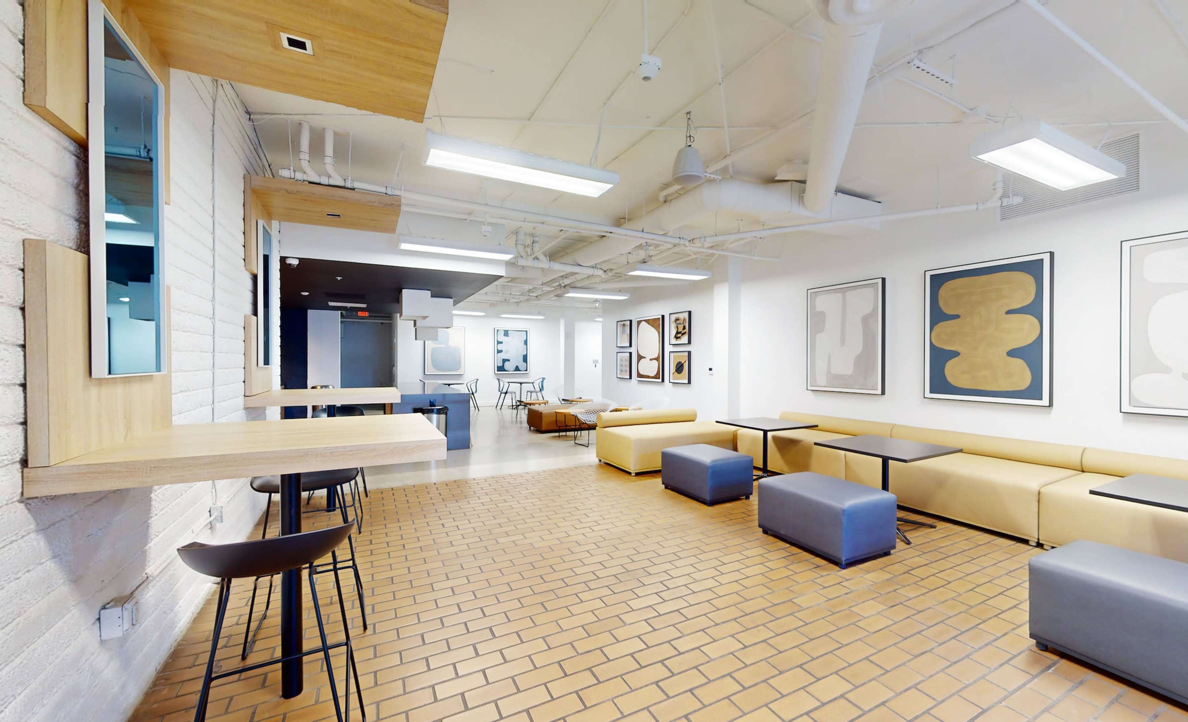 A spacious modern interior with a seating area featuring beige couches, blue ottomans, and an array of framed artwork on the walls.