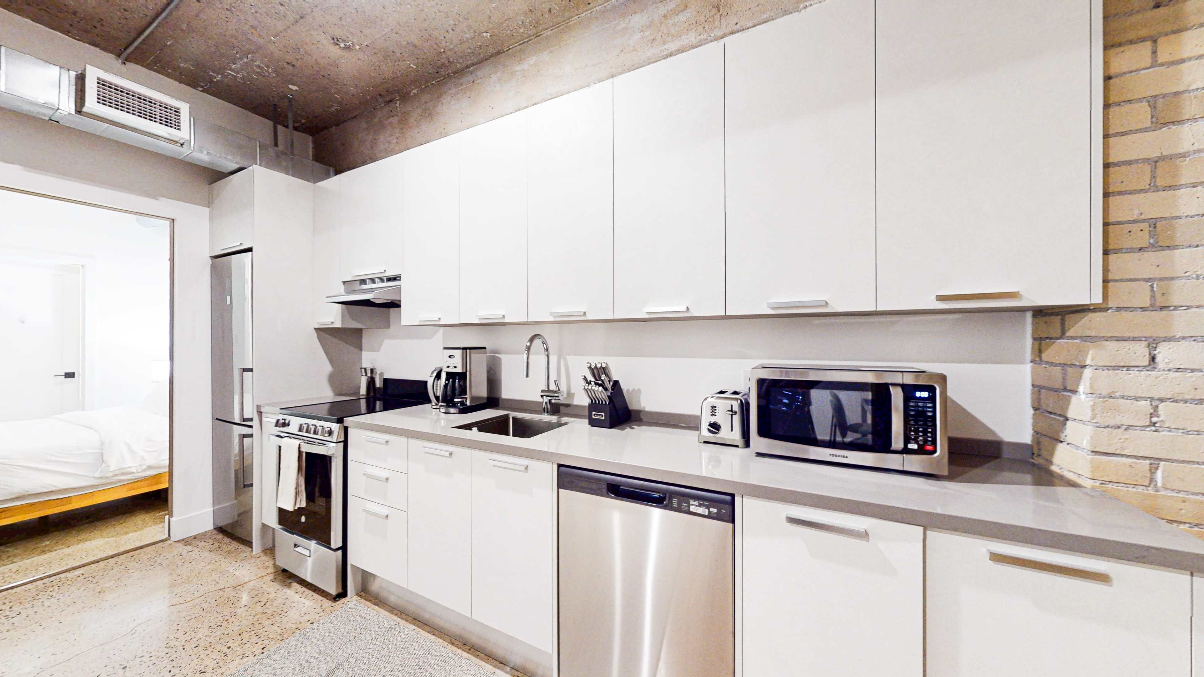 The image shows a modern kitchen with sleek white cabinetry, stainless steel appliances, and a gray countertop.