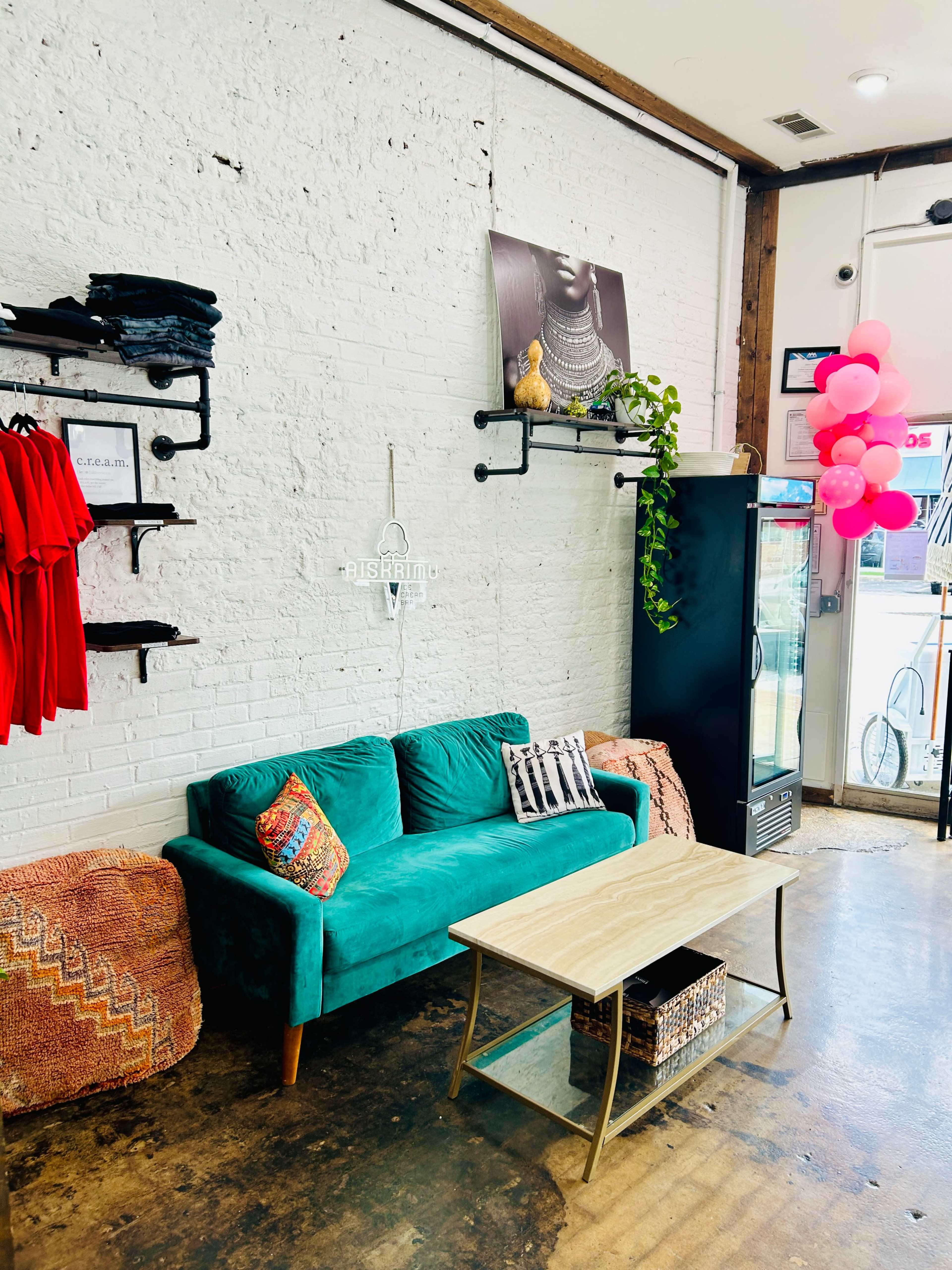 The image shows a retail space with a teal couch, a wooden coffee table, and red clothing displayed on shelves against a white brick wall.