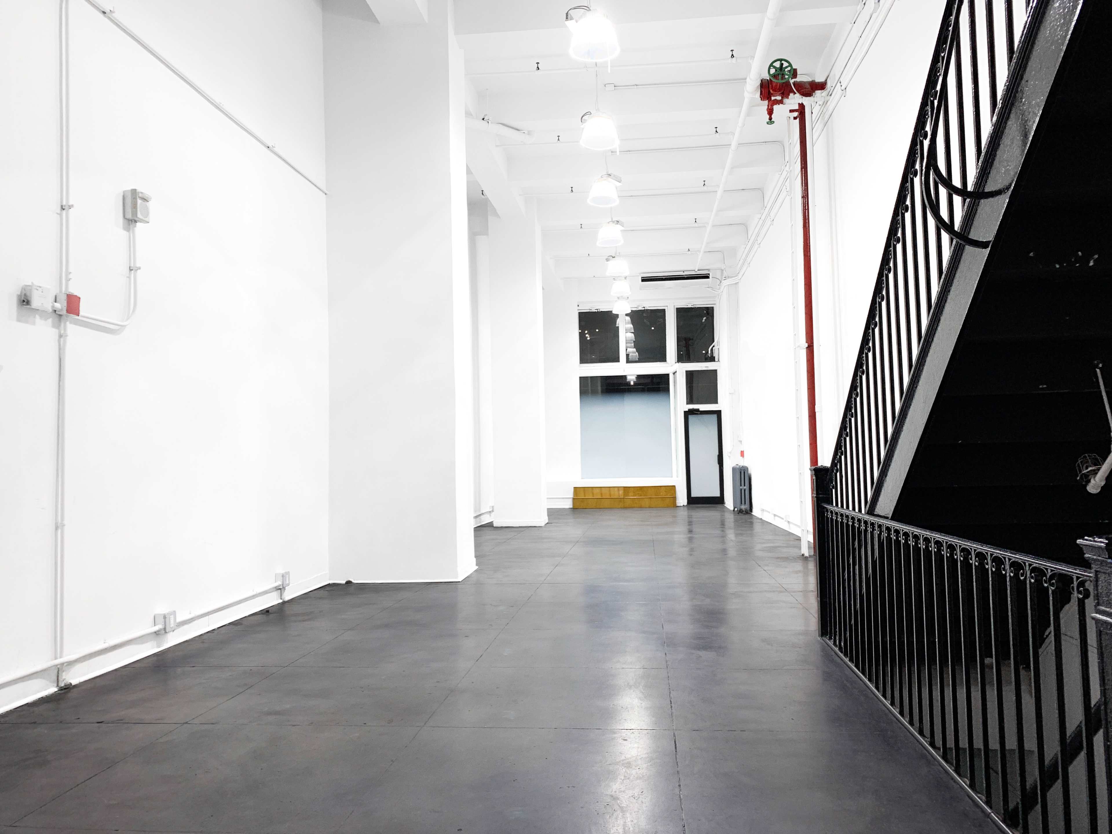 A spacious, white-walled interior with a black staircase on the right and large windows at the far end.