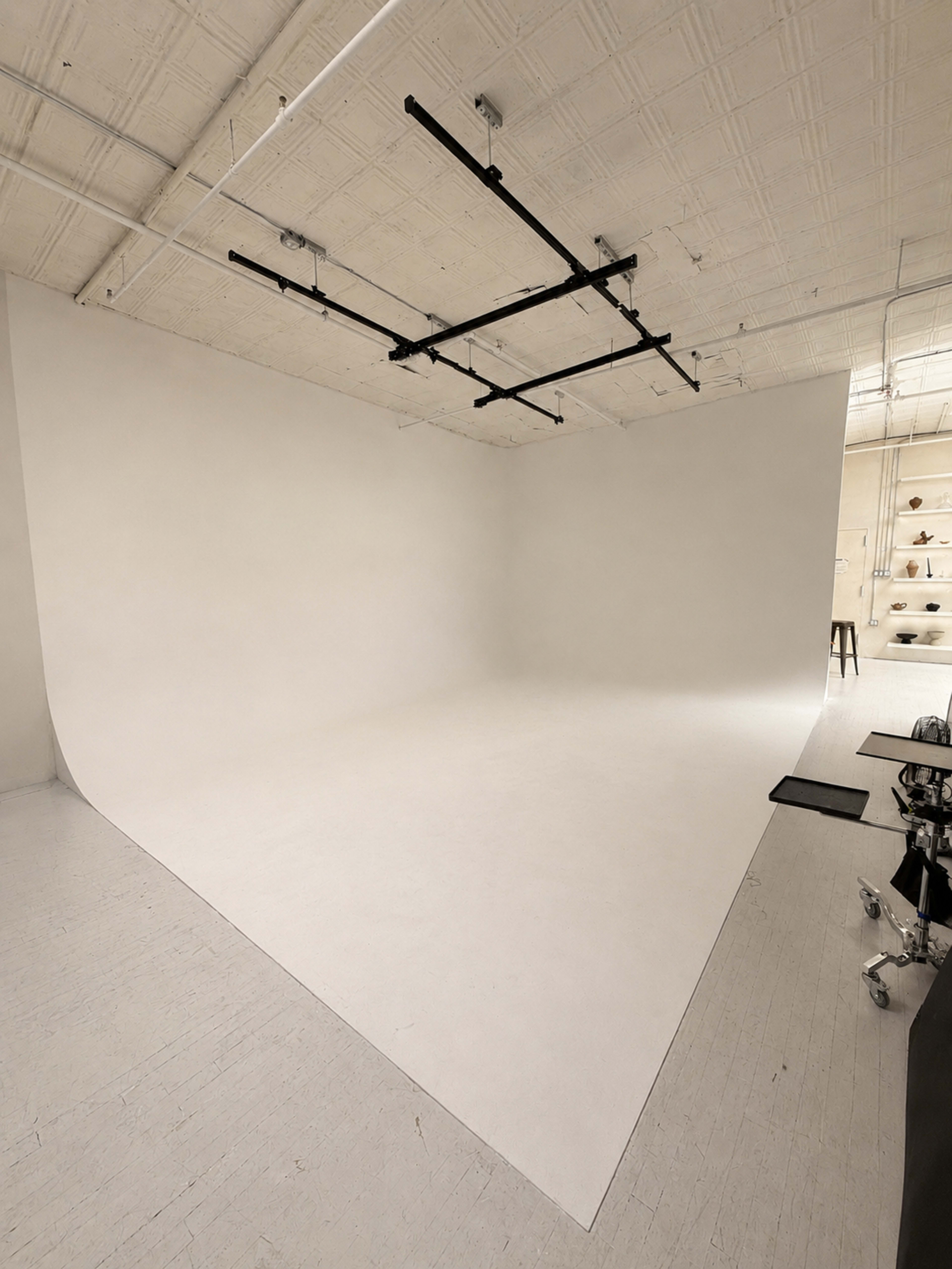 The image shows a wide, empty studio space with a seamless white backdrop and exposed ceiling beams.