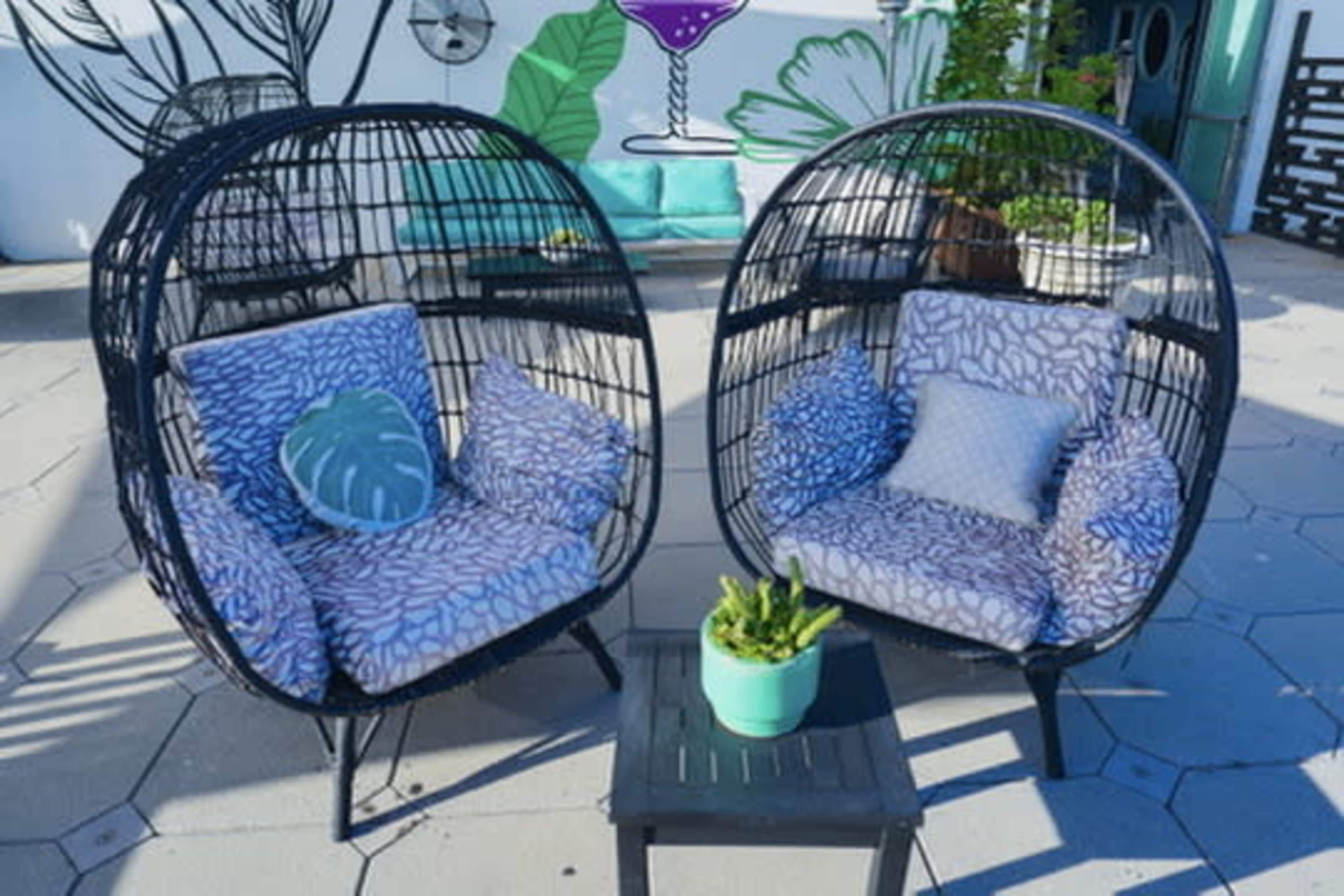 The image shows two round, wicker chairs with patterned cushions set beside a small table in an outdoor space decorated with tropical designs.