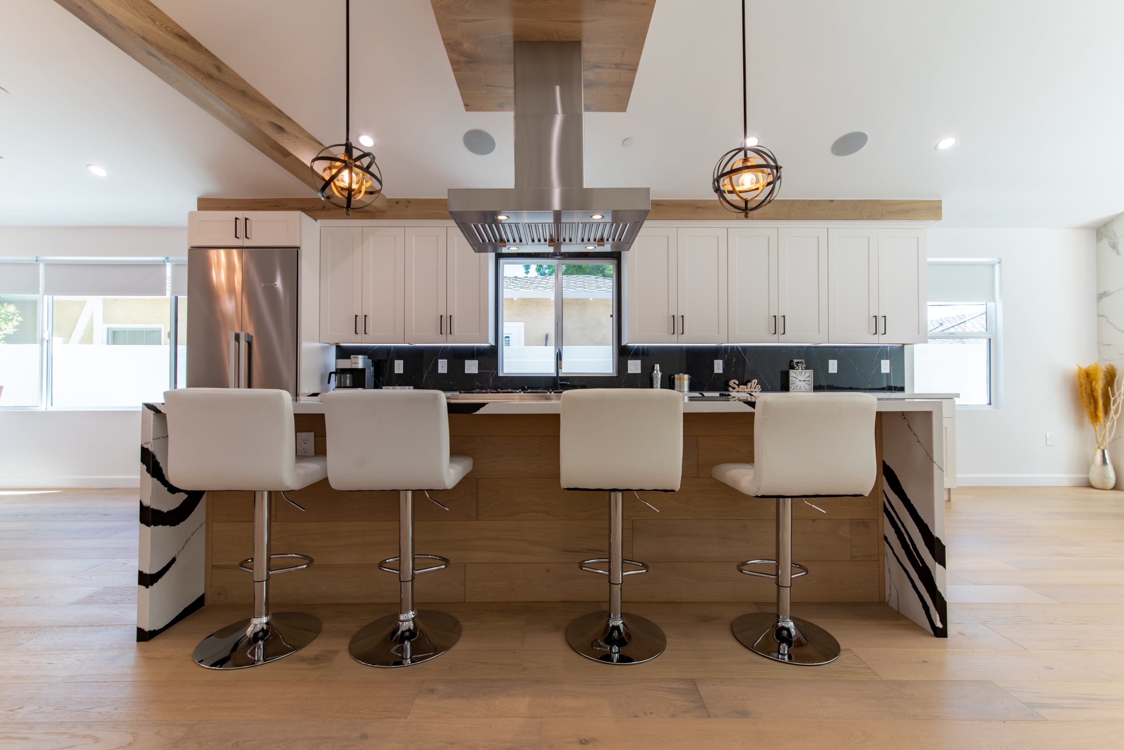 The image shows a modern kitchen with white cabinets, a wooden island, and three bar stools arranged around it.