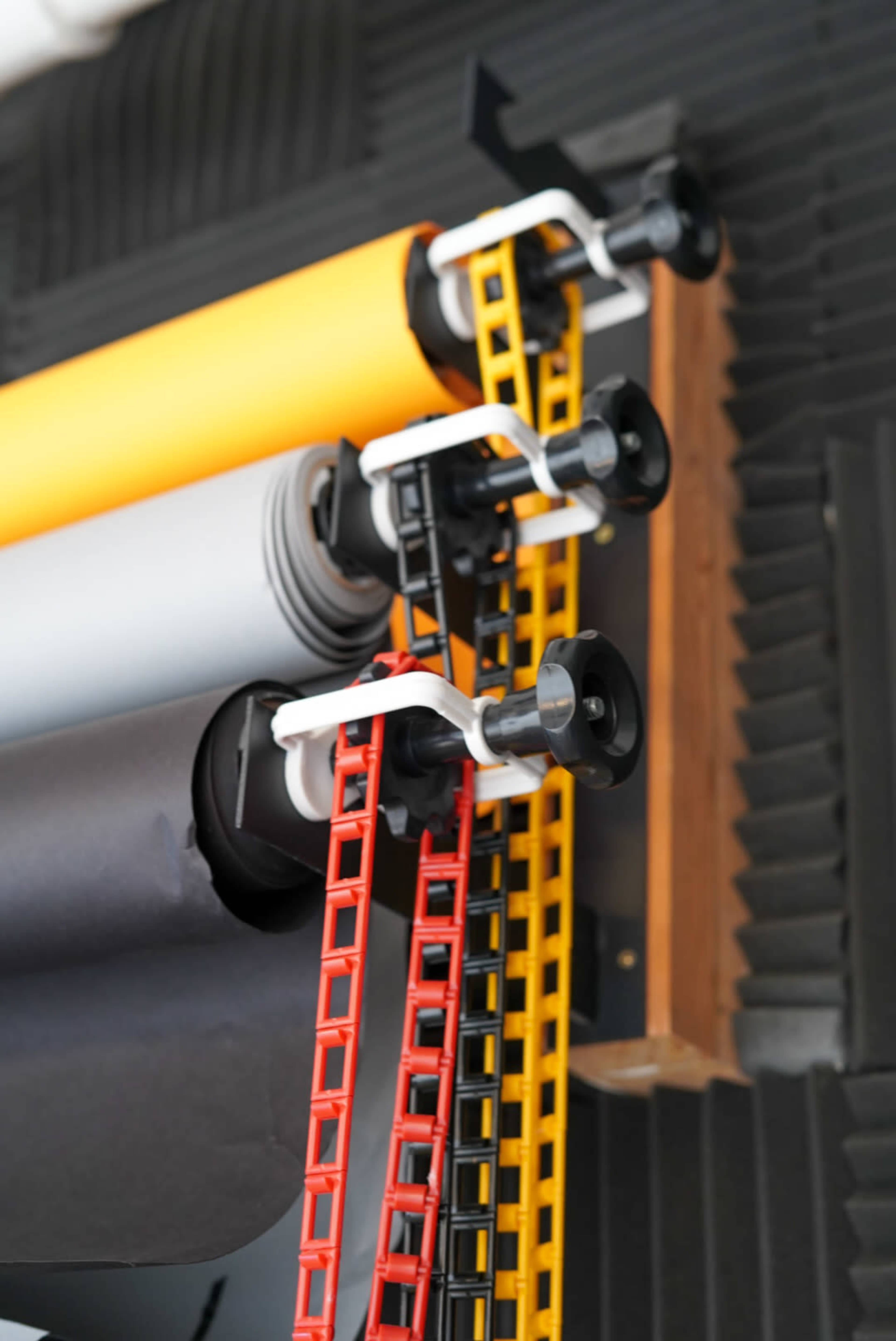 A vertical arrangement of colored backdrop rolls mounted on a wall, with support clips and ladders for adjusting the backgrounds.