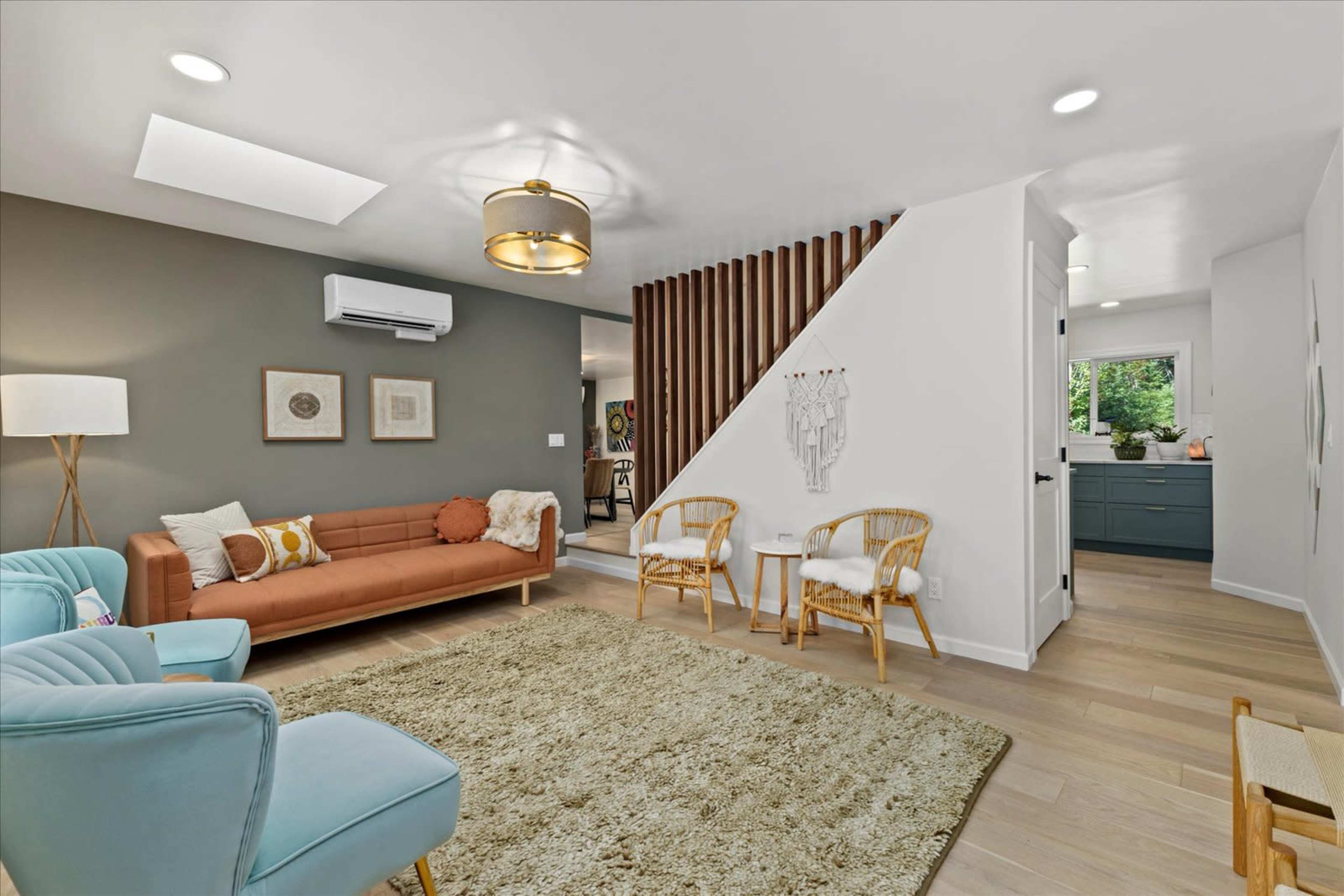 A modern living room features a brown sofa, light blue chairs, and wooden accents, with a staircase leading to another area.