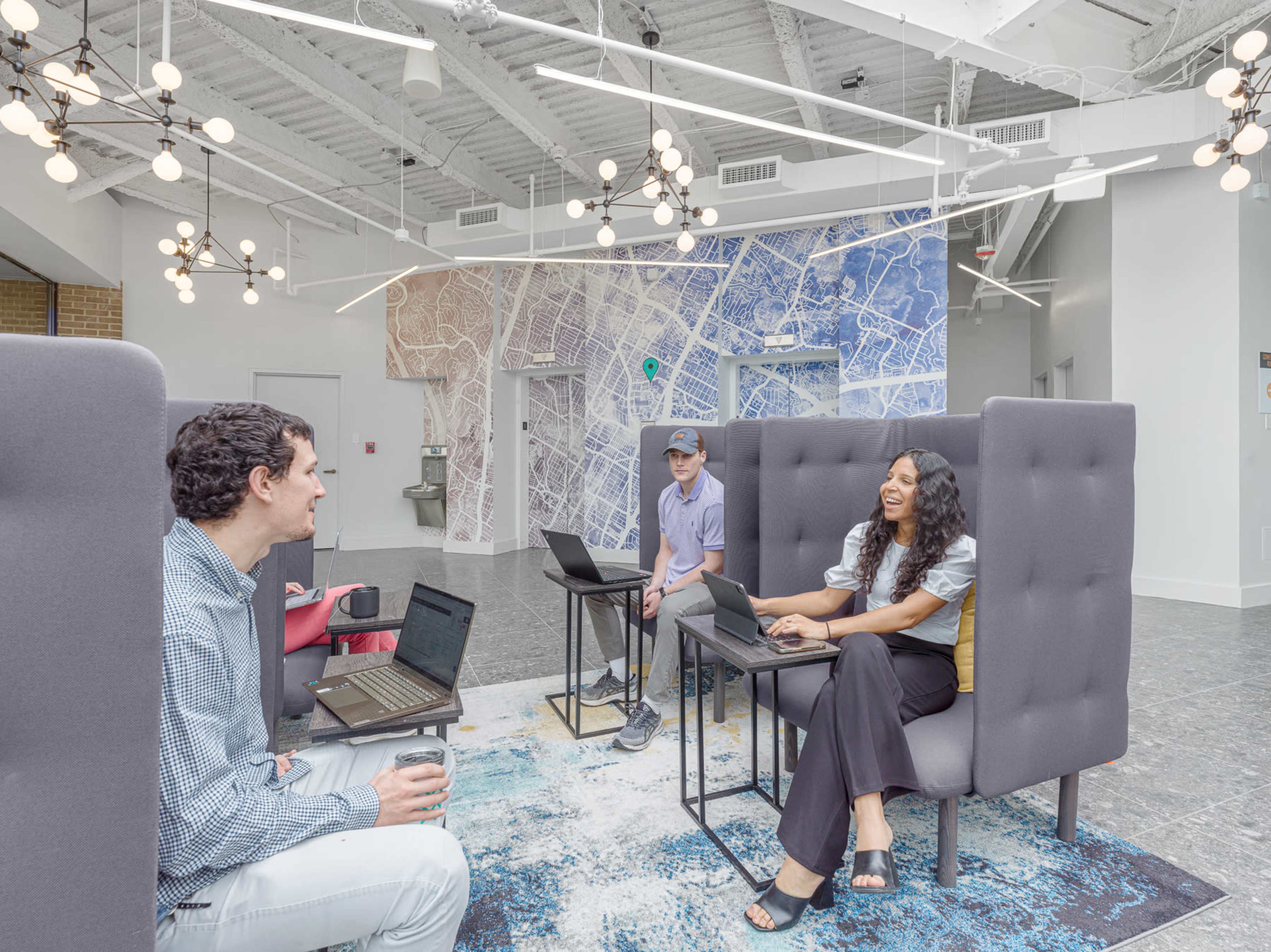 Three people are seated in a modern office space with decorative partitions, collaborating while using laptops on small tables.
