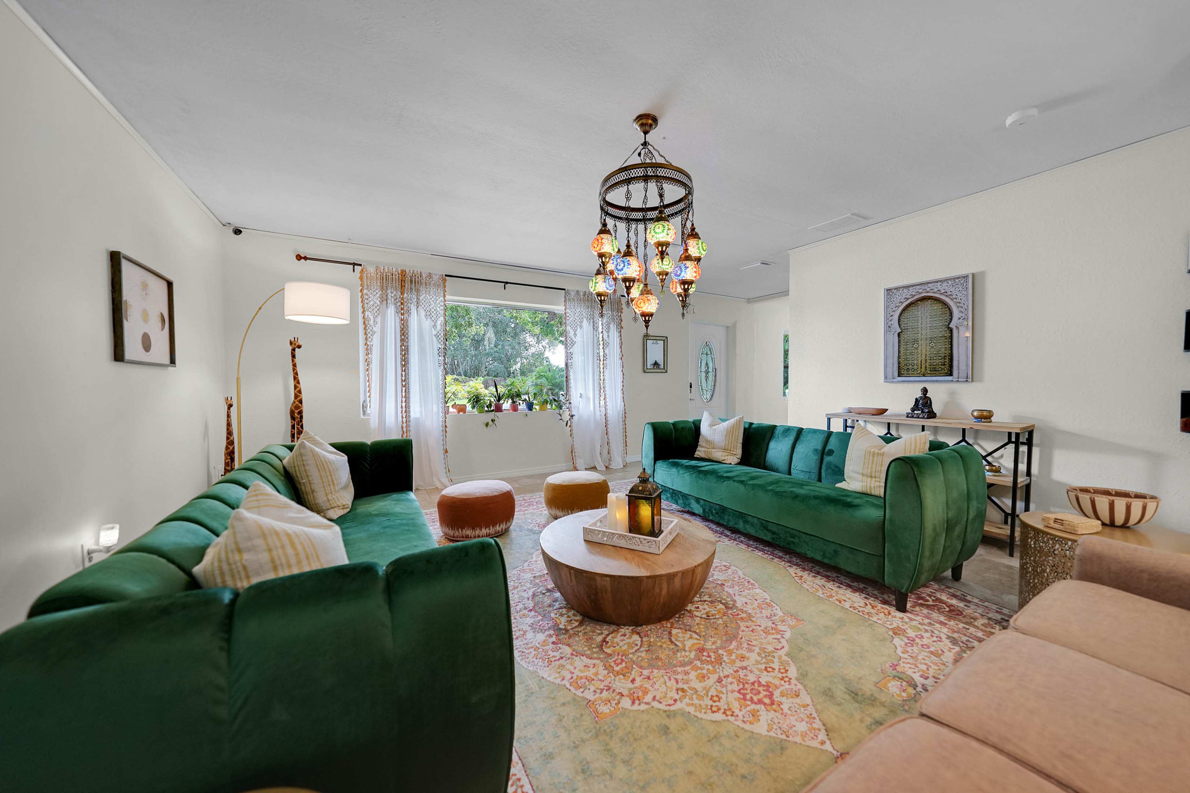 A spacious living room features two green sofas, a round wooden coffee table, and a decorative chandelier hanging overhead.
