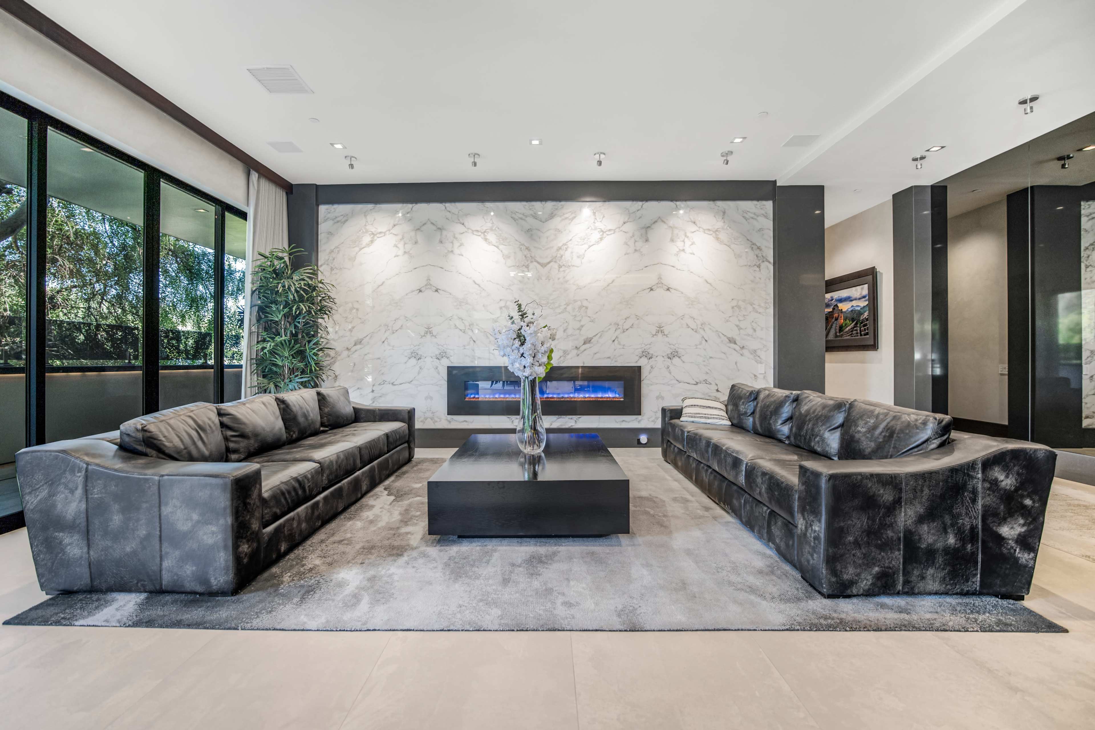 The image shows a modern living room with two dark sofas facing a sleek coffee table and a wall featuring a stone fireplace.