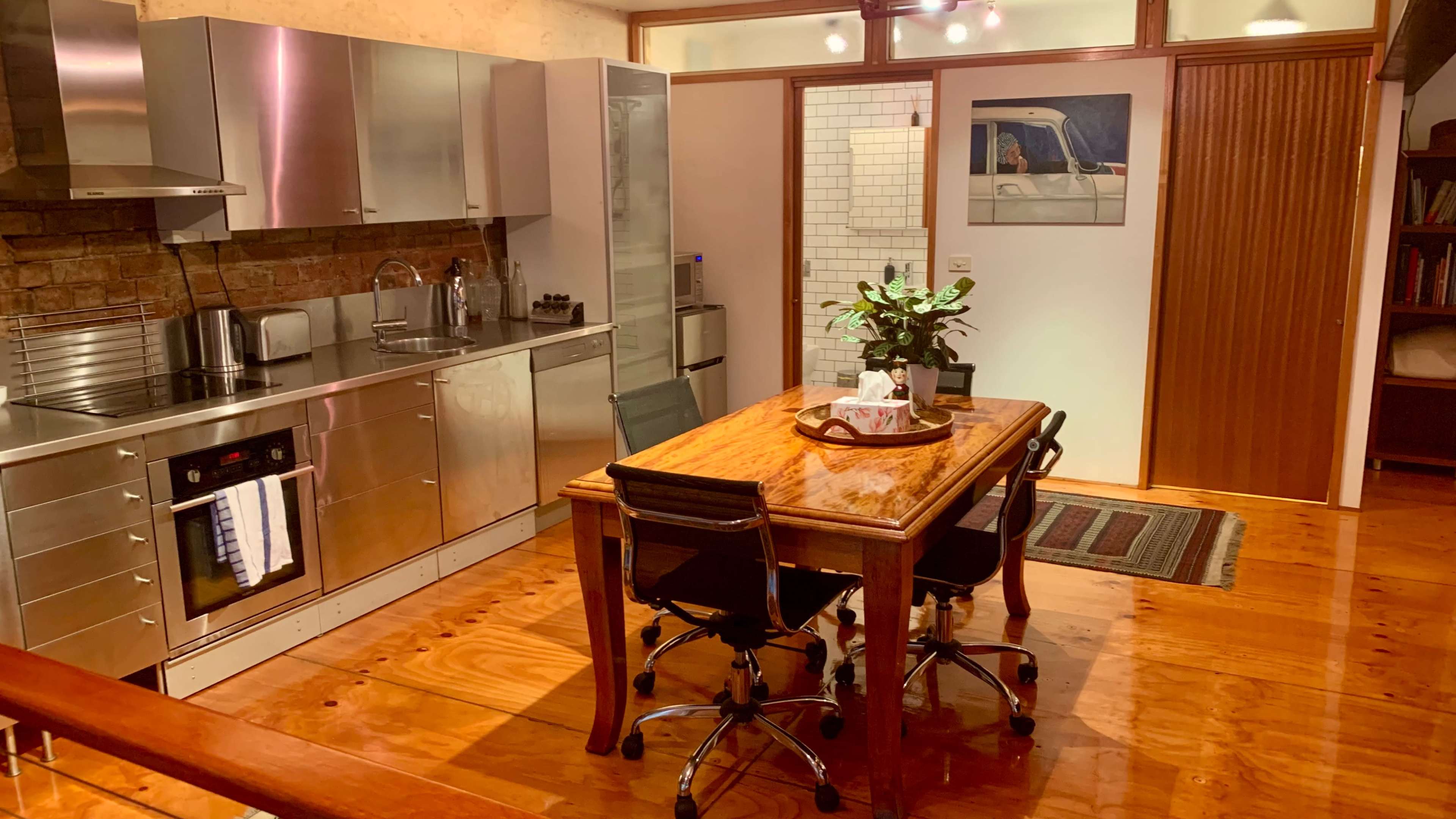 A modern kitchen features stainless steel appliances, a wooden dining table with chairs, and a door leading to a pantry area.