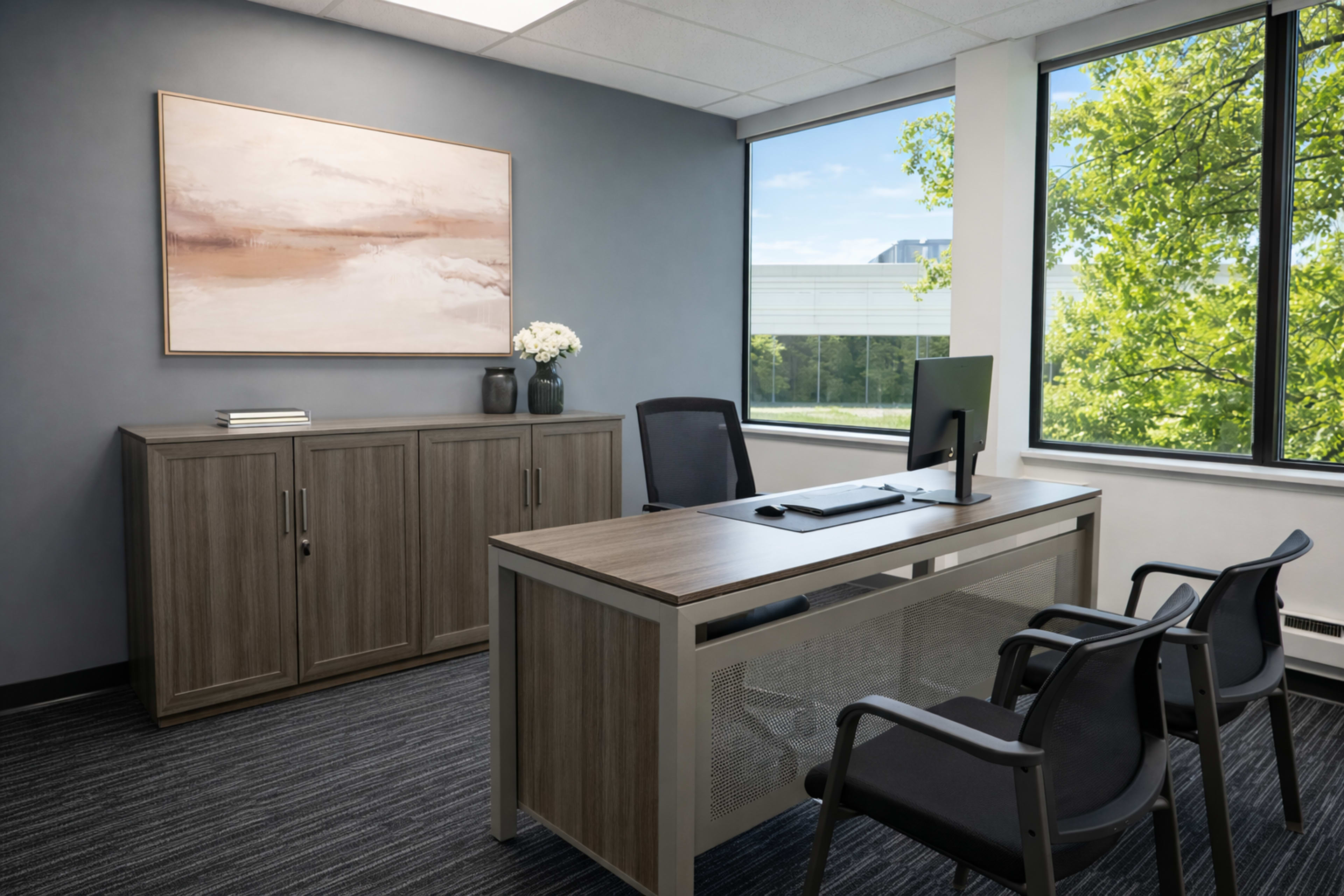 The image shows a modern office space with a desk, a computer, a cabinet, and three chairs arranged near large windows overlooking greenery.
