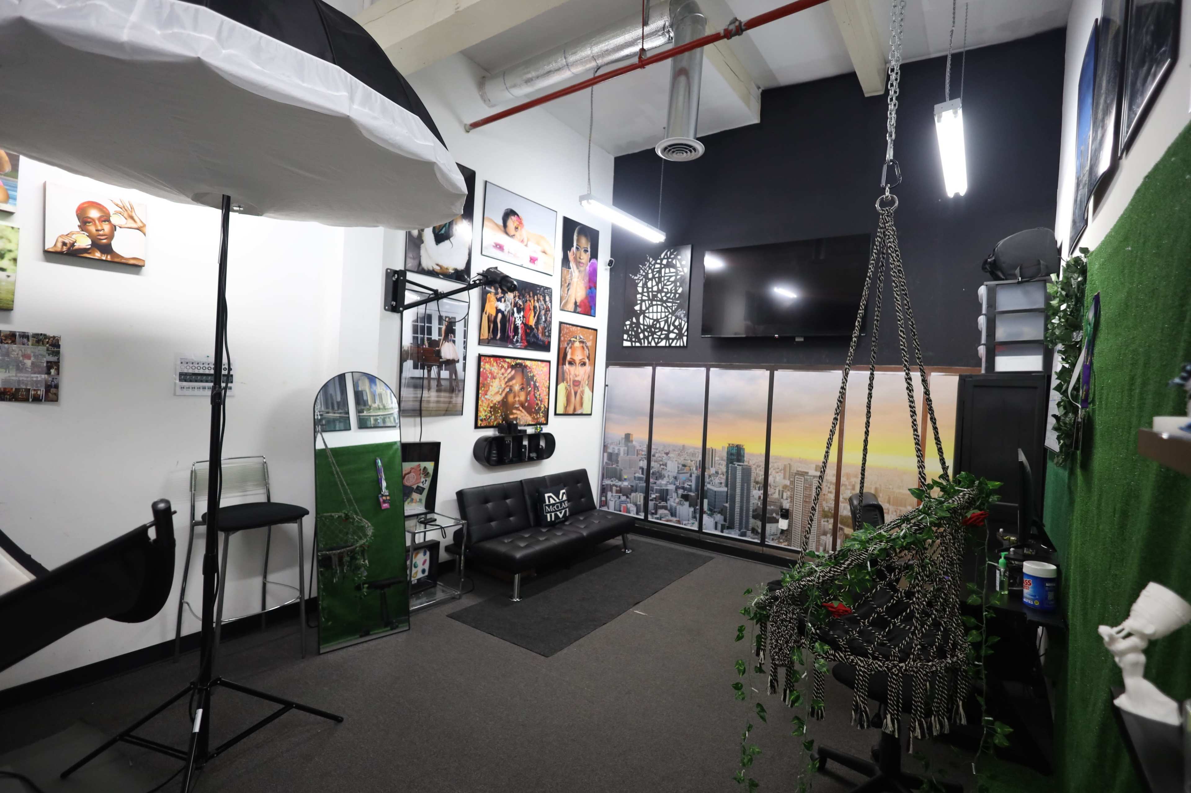 The image shows a photography studio with various photographs on the walls, a hair styling chair, a large mirror, and a decorative plant hanging from the ceiling.