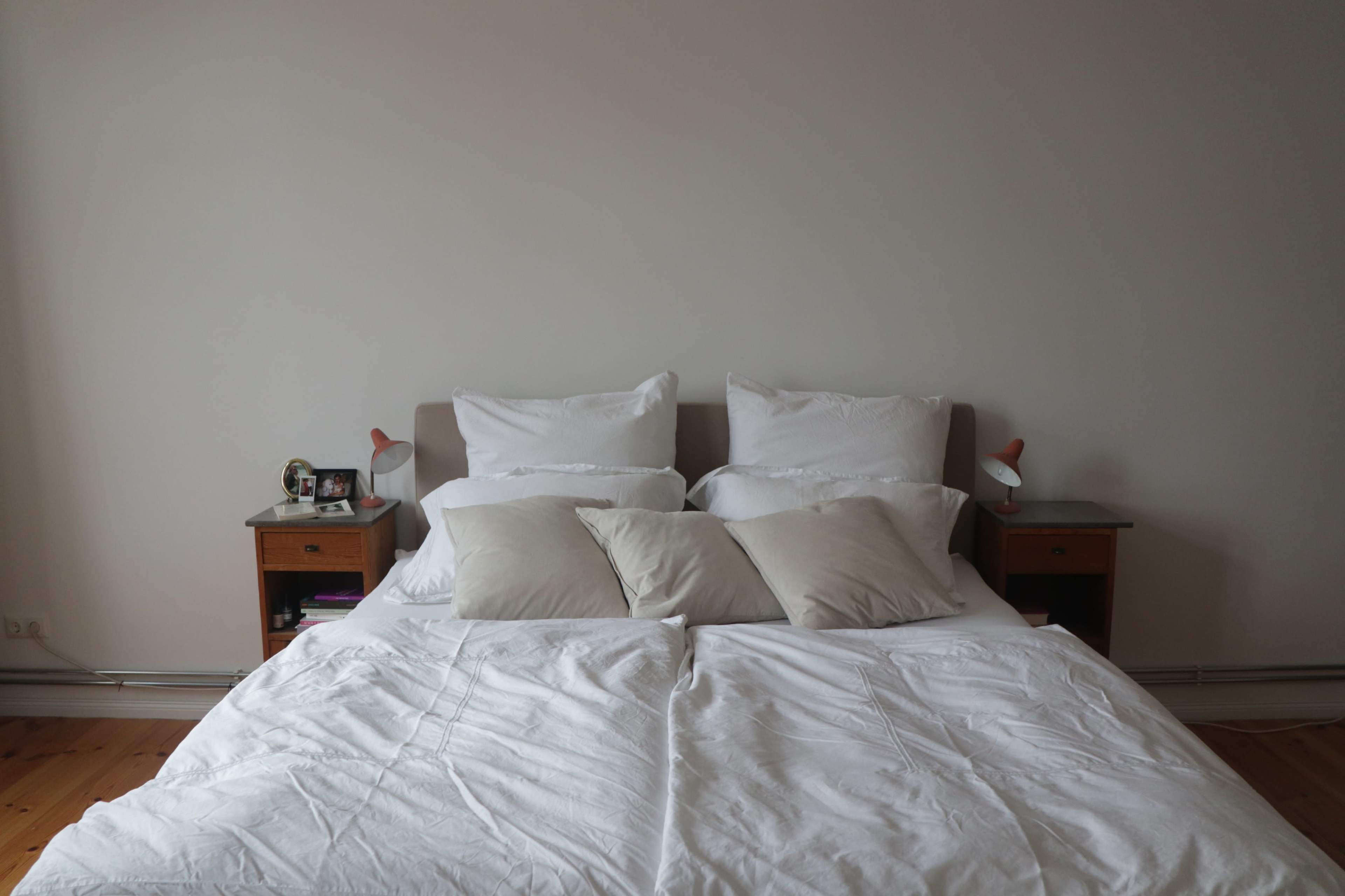 A neatly made bed with white linens and two beige pillows is positioned against a plain wall, flanked by two wooden nightstands.