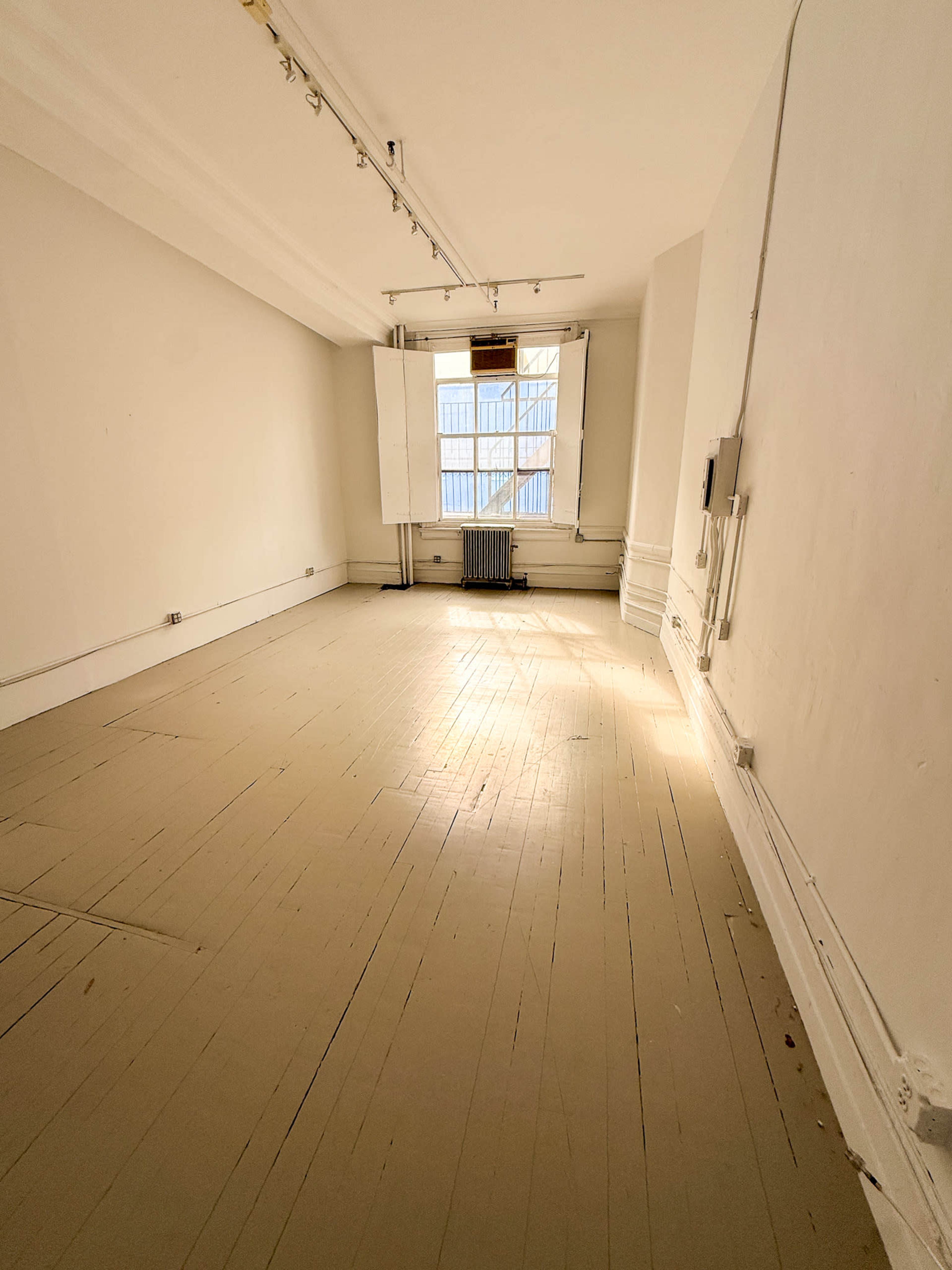 A vacant room with wooden flooring and a large window allowing natural light to enter.