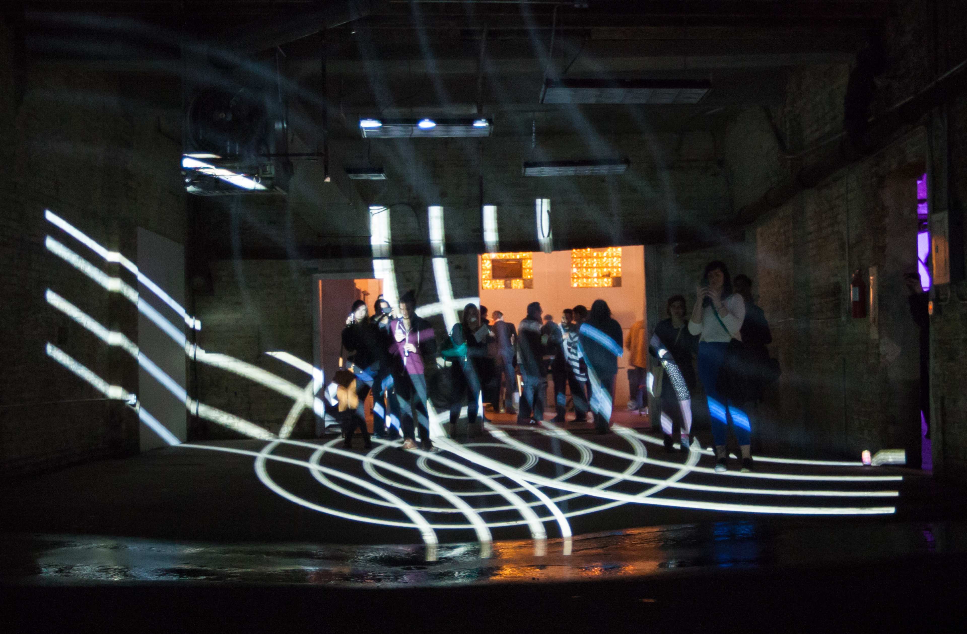 People walk through a dimly lit industrial space with patterned light projections on the floor.