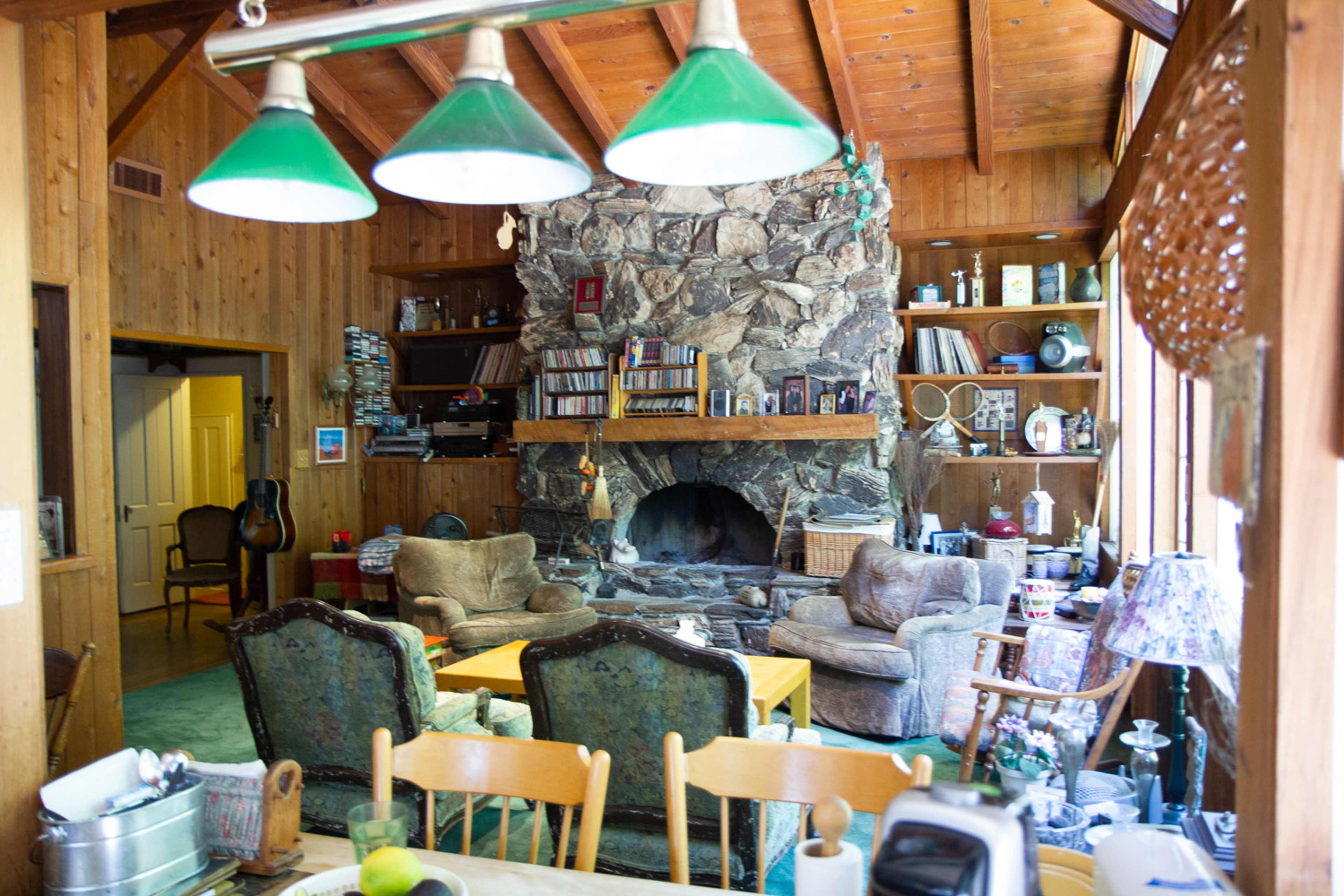 A rustic living room with a stone fireplace, wooden walls, and comfortable seating arranged around a coffee table.