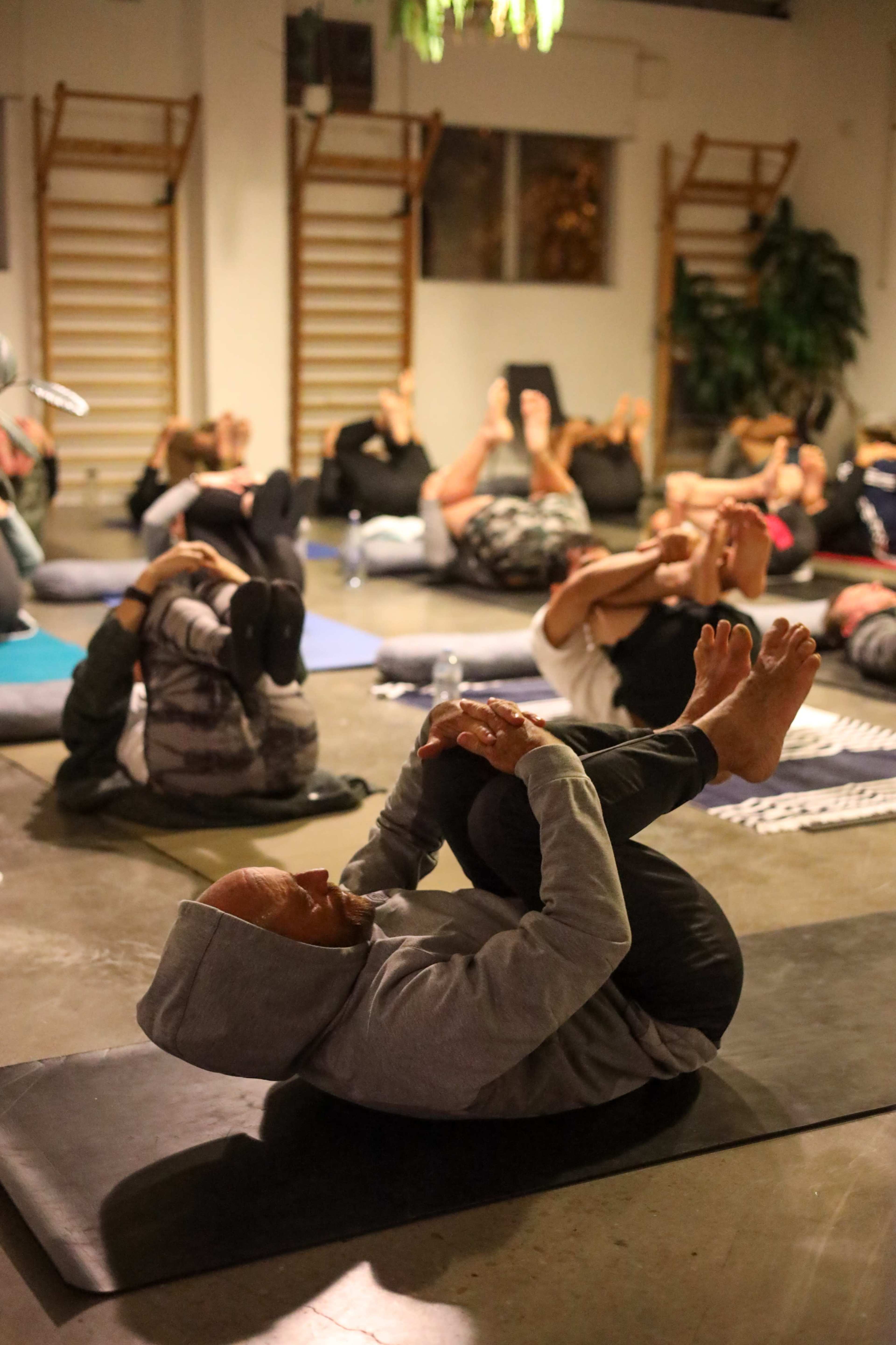 A group of people is practicing yoga in a studio, performing a pose while lying on mats.
