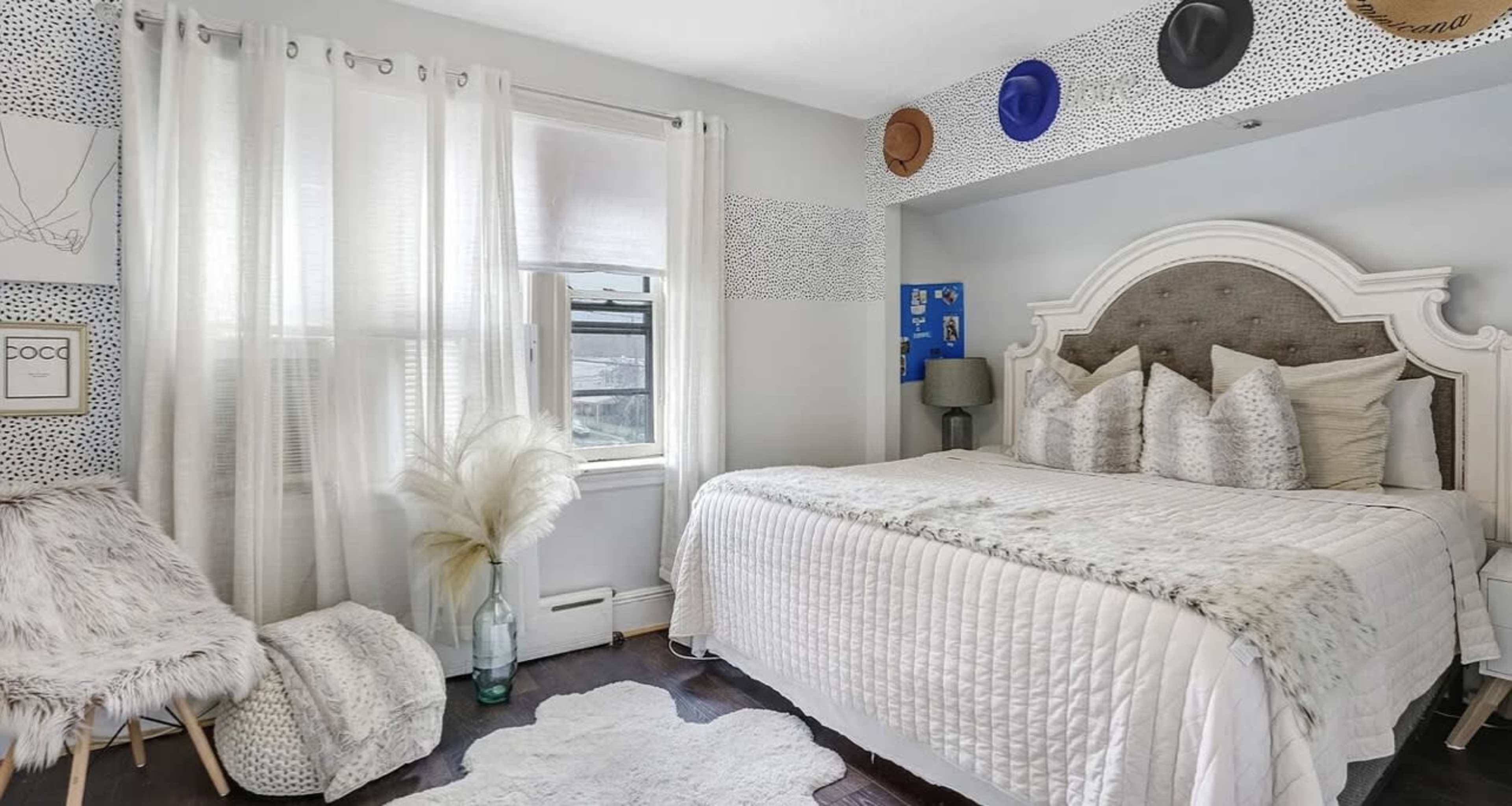 The bedroom features a large bed with decorative pillows, a reading nook with a cozy chair, and light-colored curtains letting in natural light.