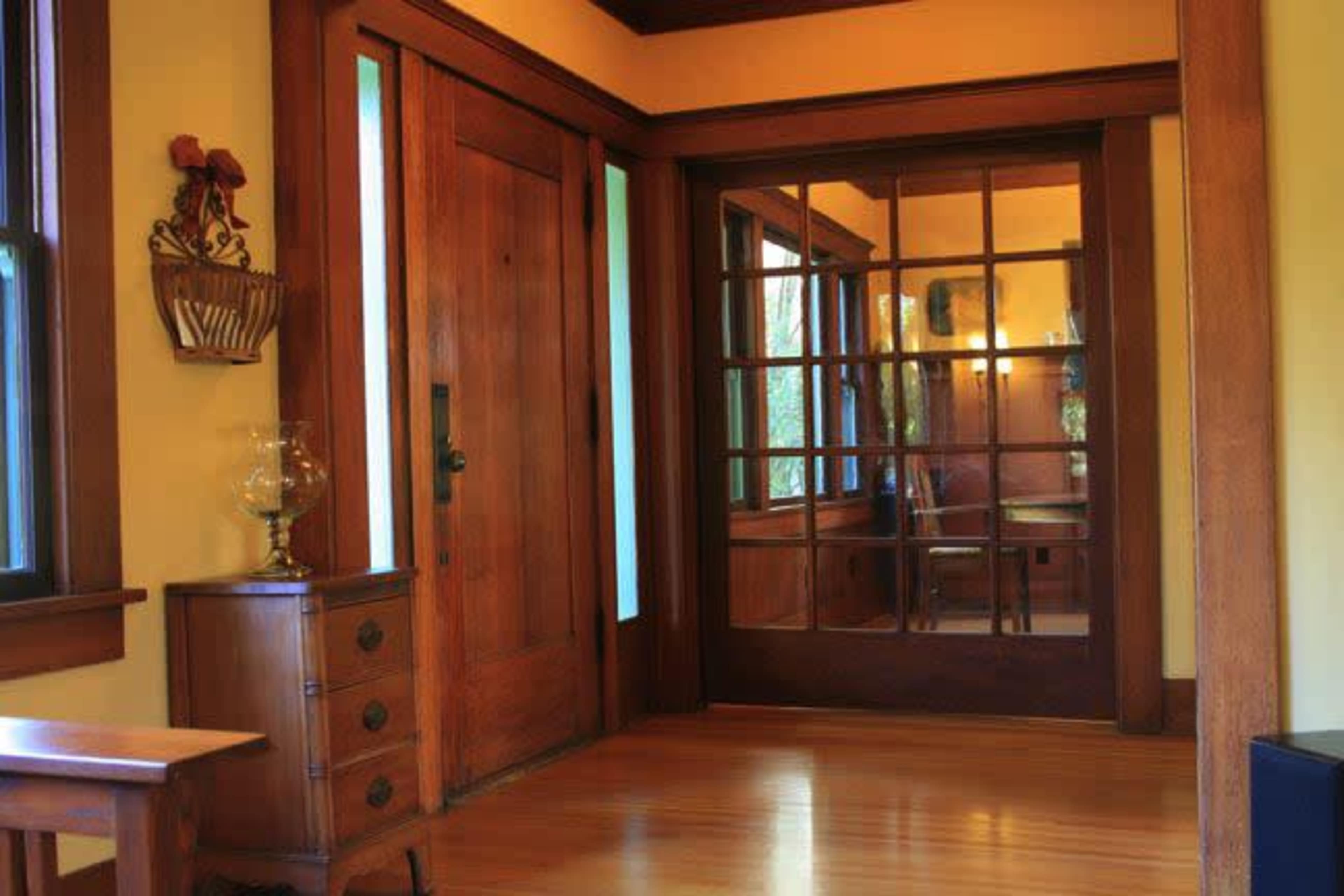 A wooden entryway with a glass-paneled door leading to a well-lit room, featuring wooden paneling and a vintage table.