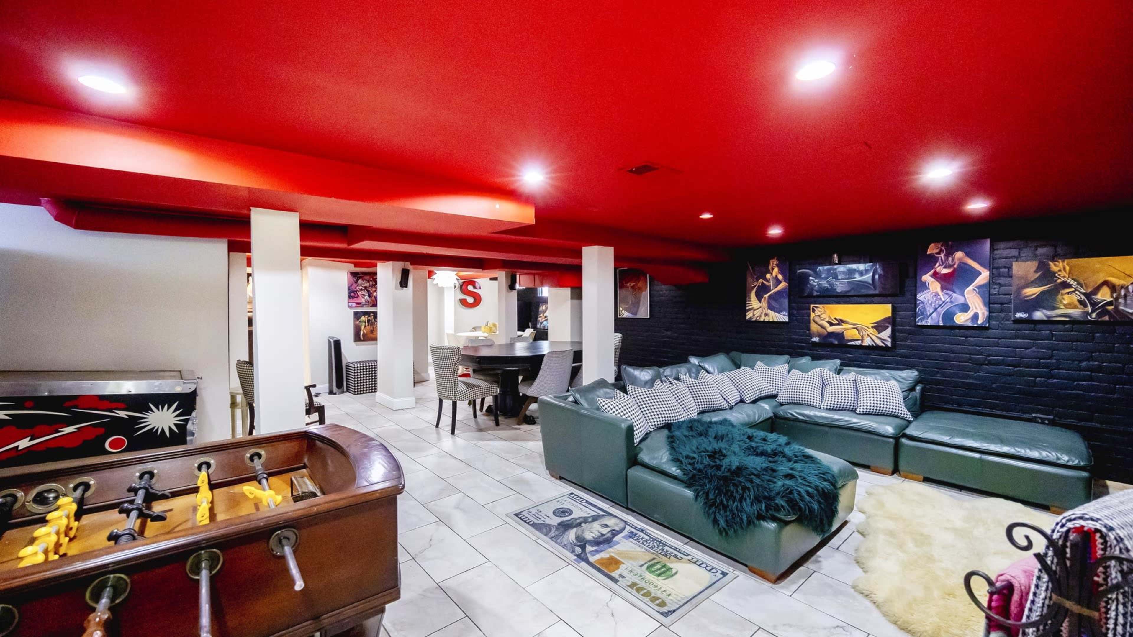 A basement recreation area with a green sectional sofa, a foosball table, and decorative artwork on the walls.