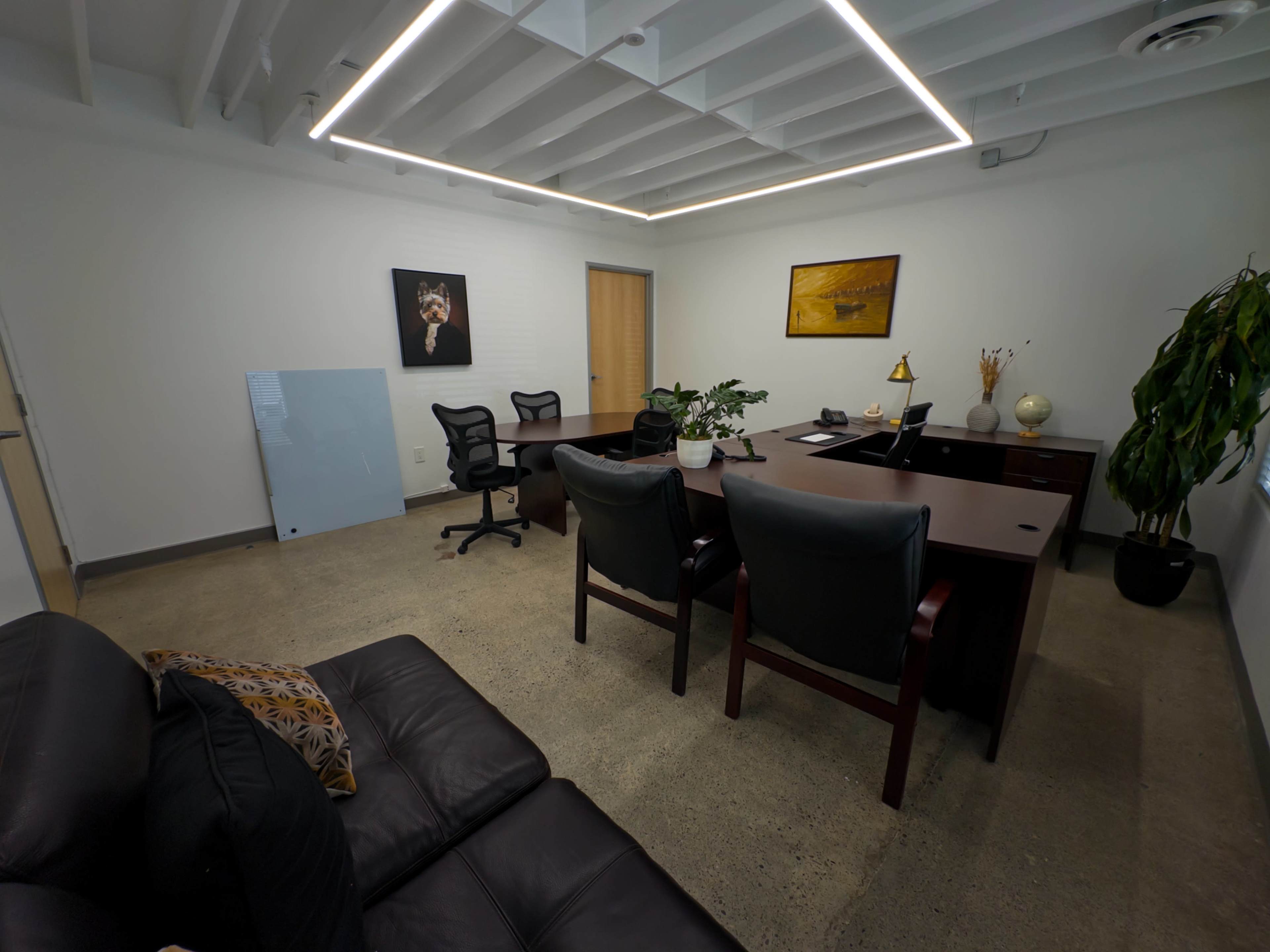 The image shows a modern office space with a large desk, two chairs, a couch, and various decorative items on the walls and desk.