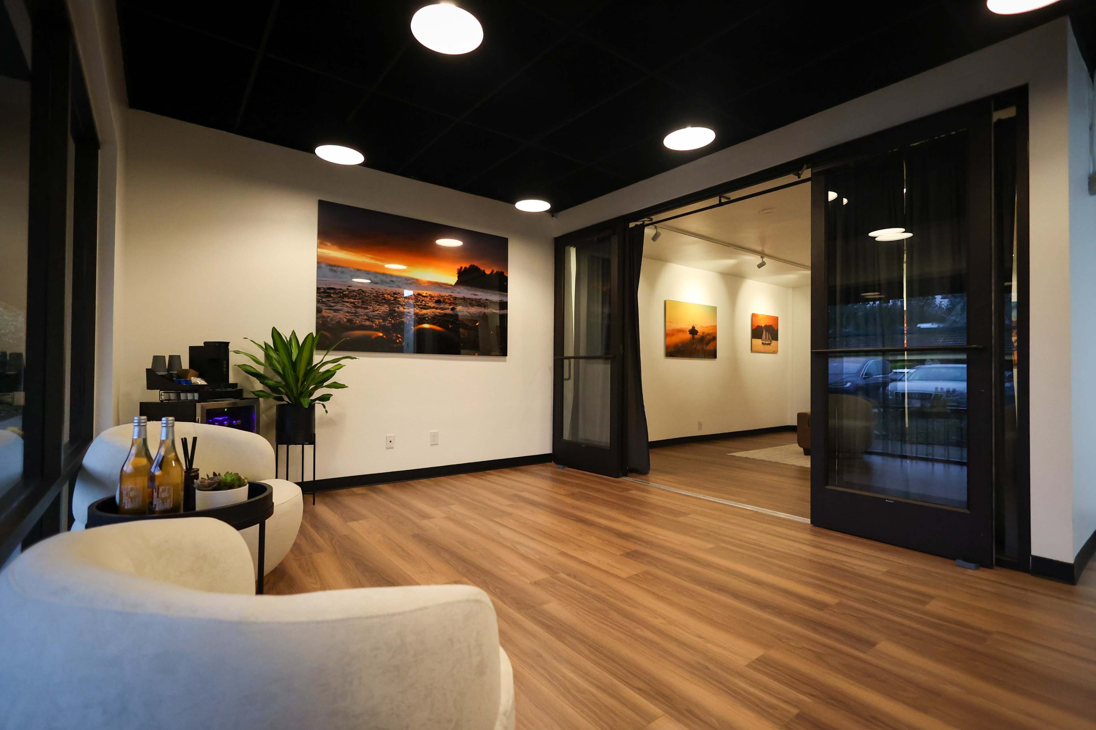 A modern interior space with hardwood floors, soft seating, and vibrant landscape paintings on the walls.