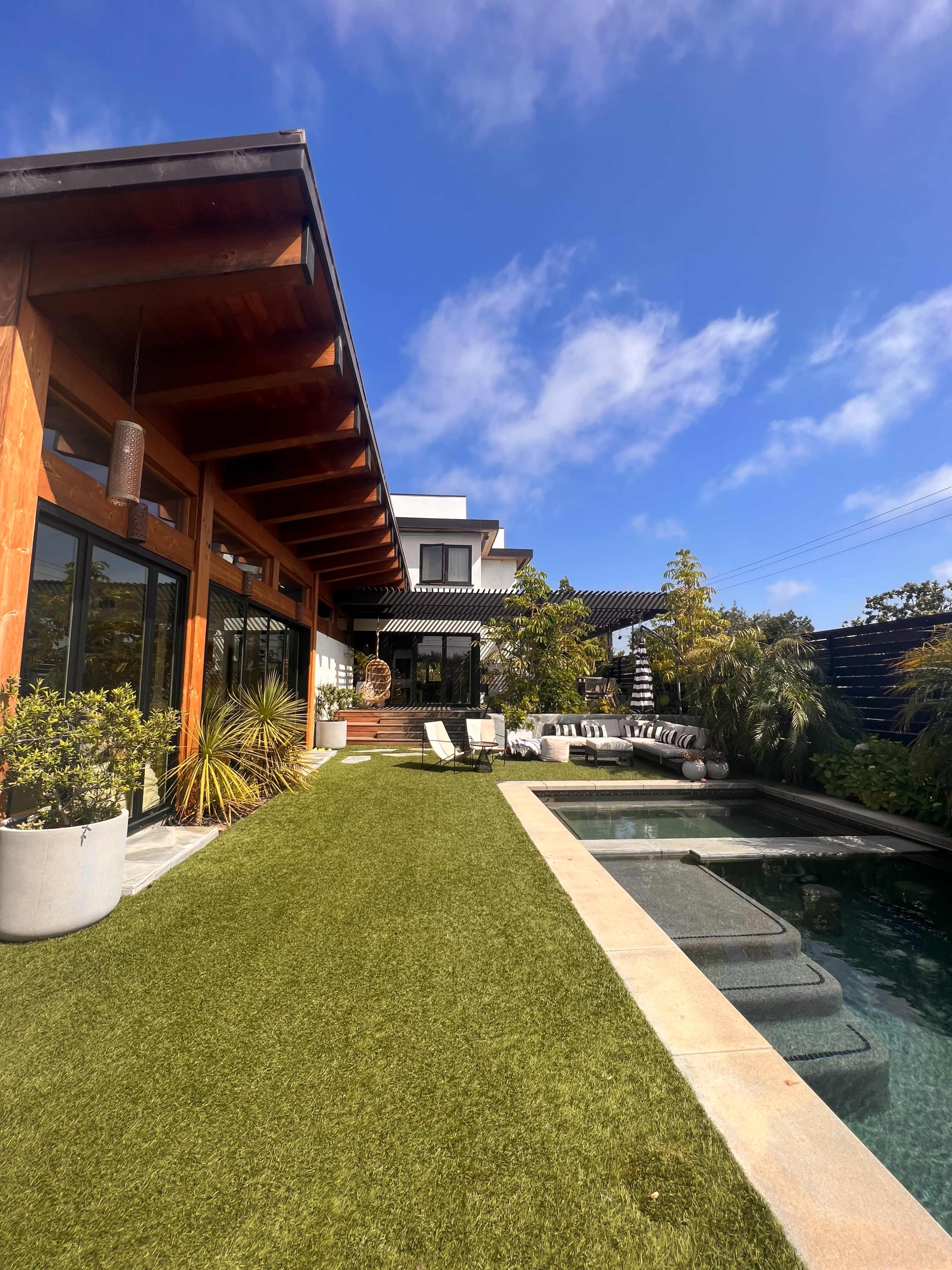 A modern home features a spacious lawn, a swimming pool, and a patio area with lounge chairs under a clear blue sky.