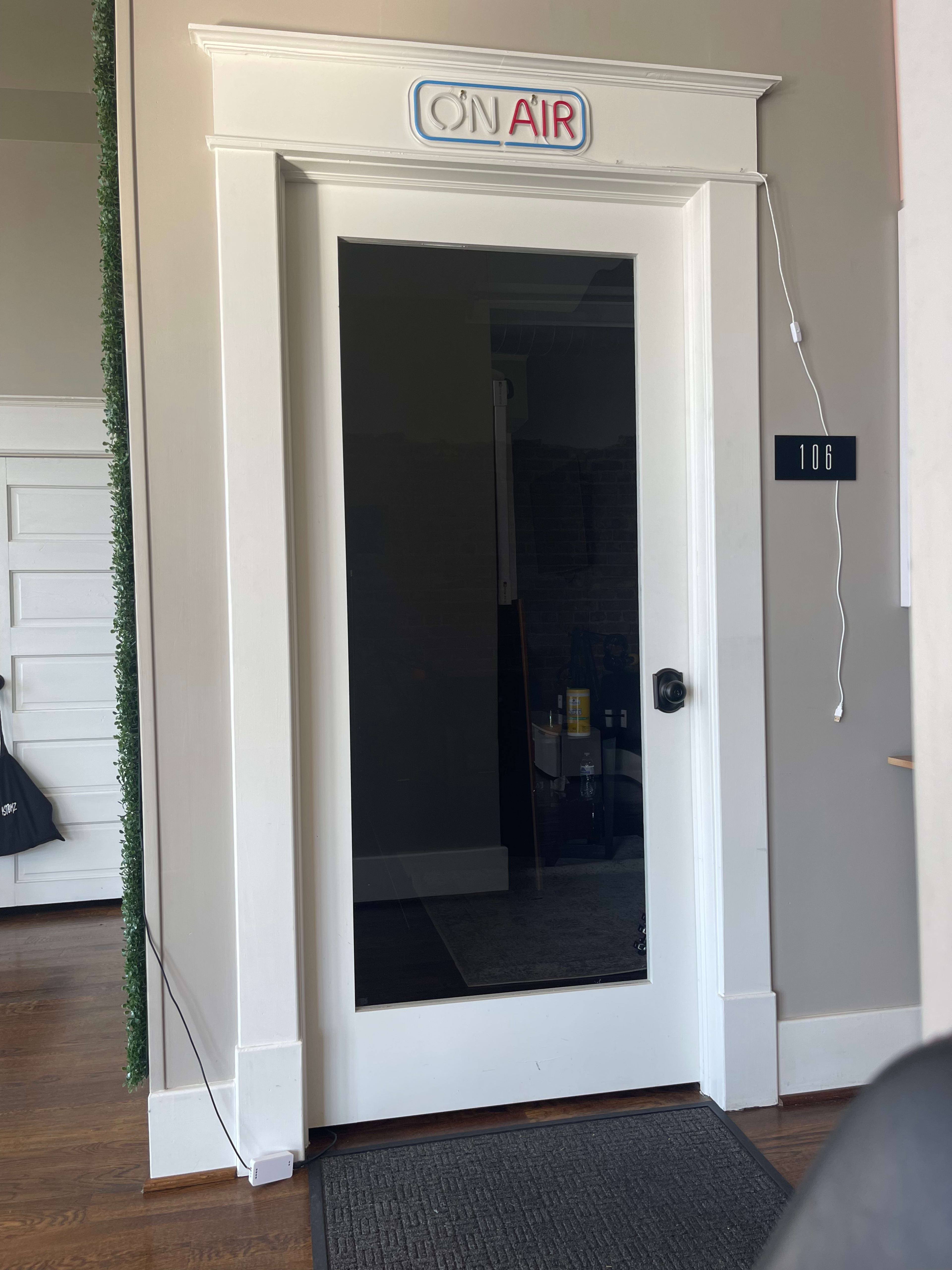 A closed door with a sign labeled "ON AIR" at the top and a room number "106" on the wall beside it.