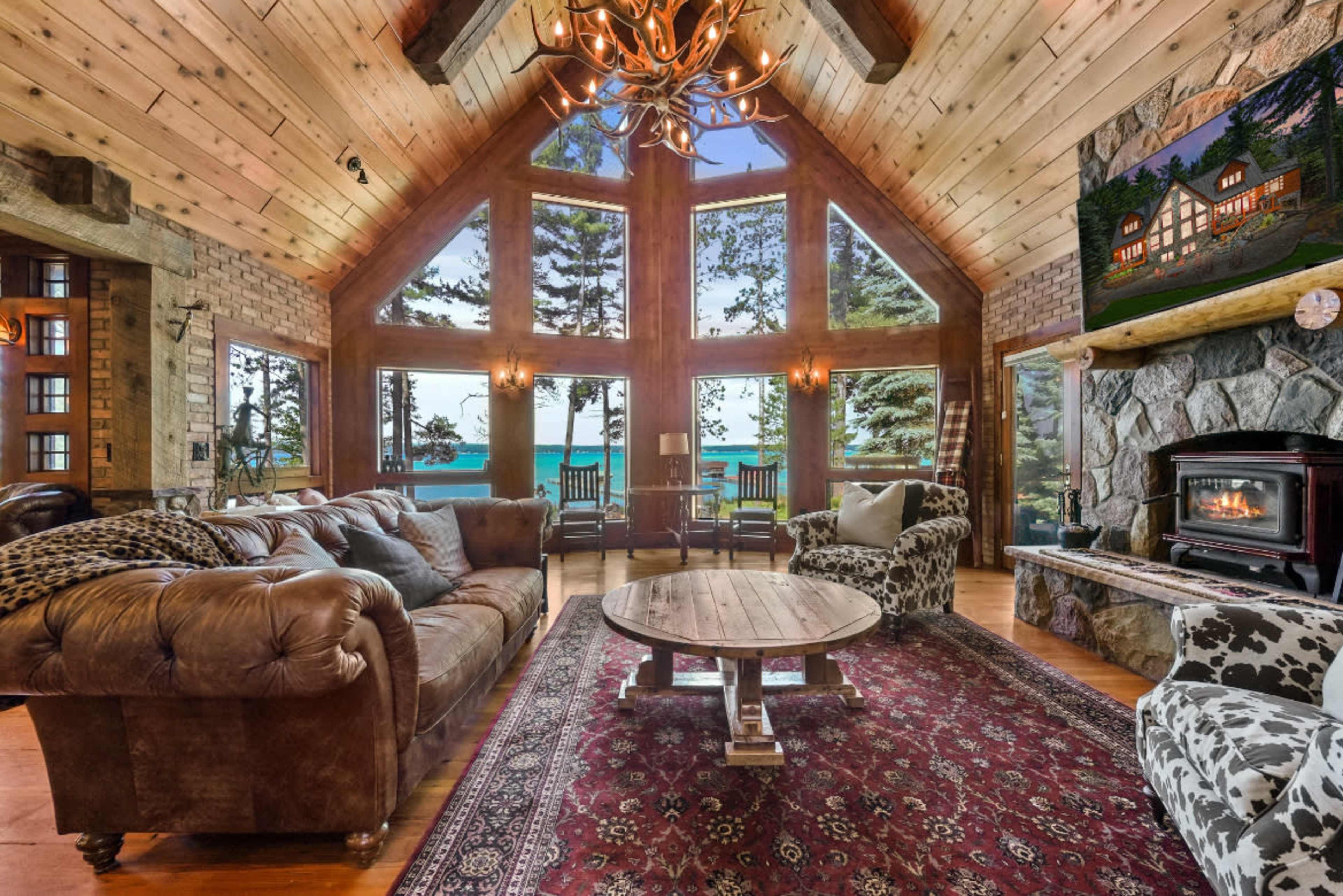 A spacious living room features large windows with a view of the lake, a stone fireplace, and rustic wooden decor.