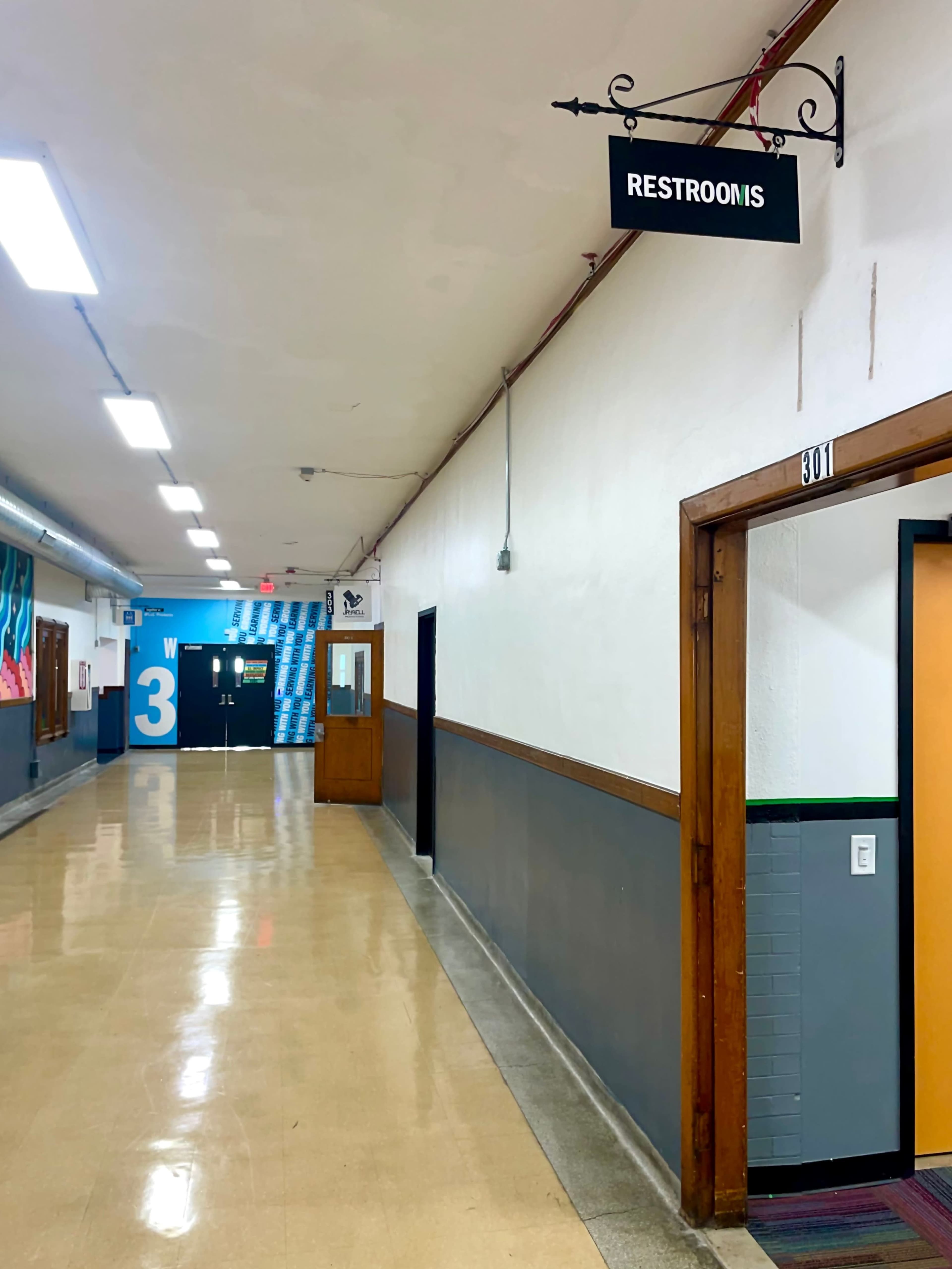 A hallway with a sign labeled "RESTROOMS" hangs above a doorway, leading to a pair of restrooms.