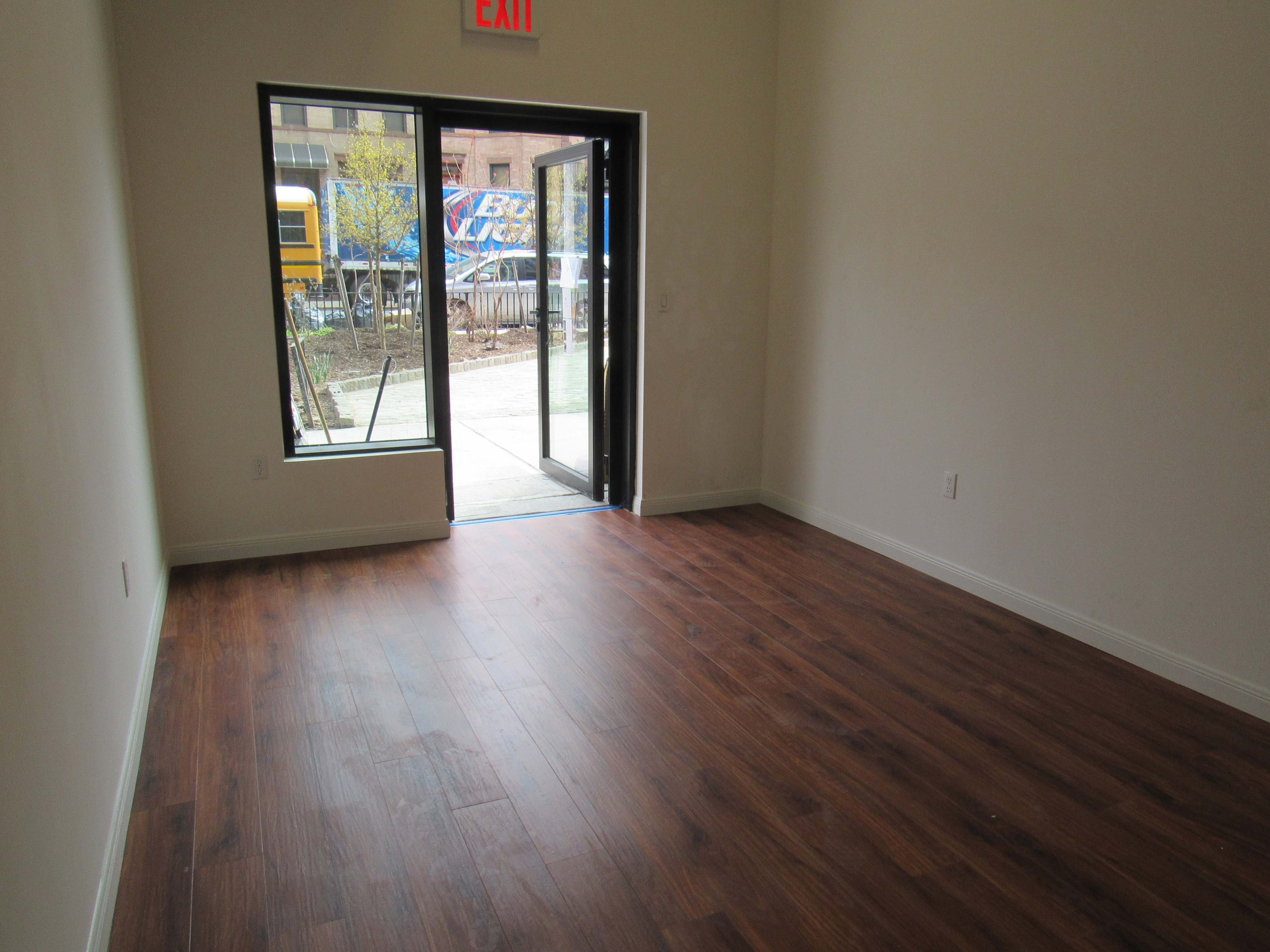 An empty room with wooden flooring and a large door leading to an outdoor area.