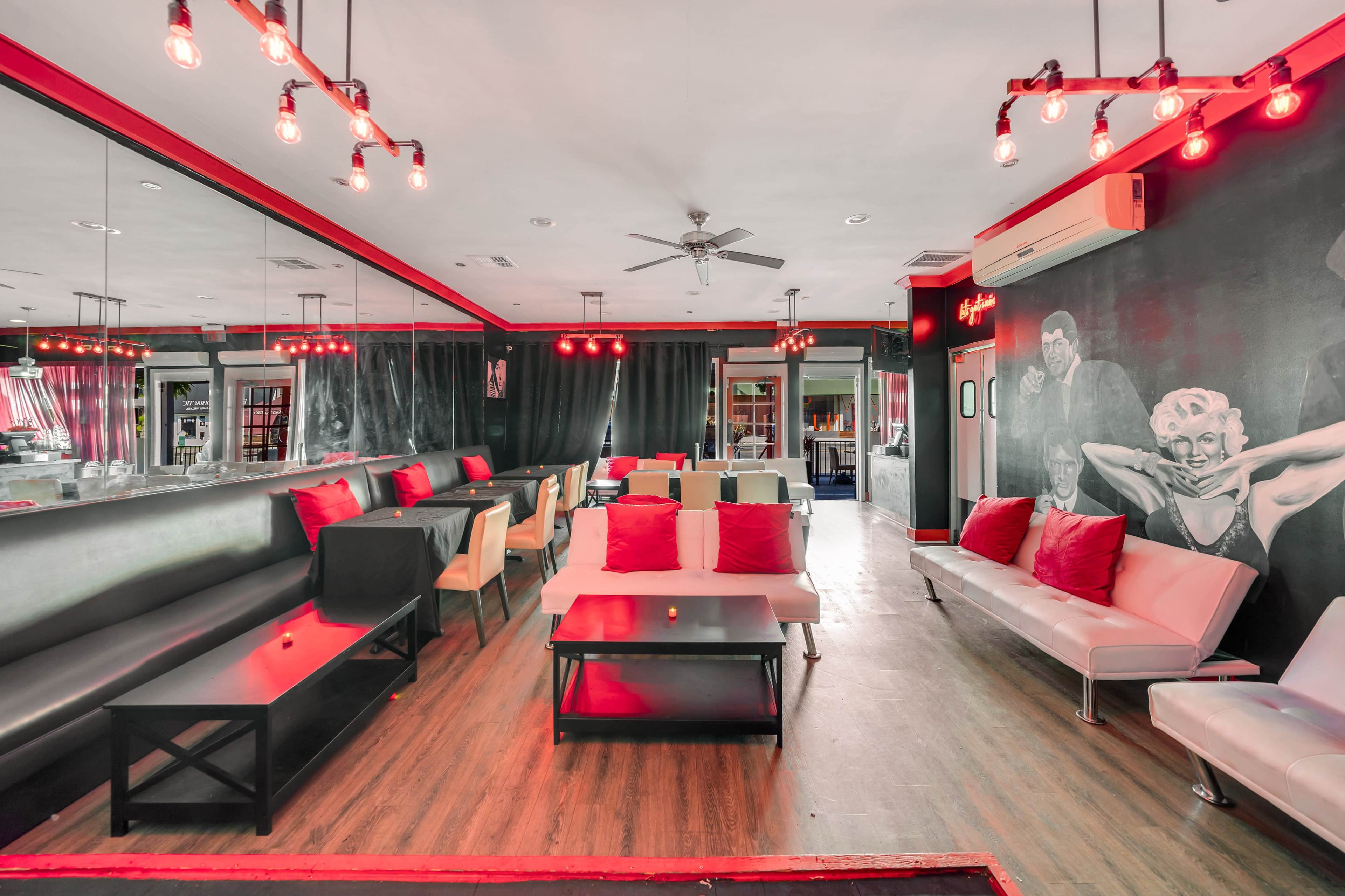 A stylish lounge area featuring black seating, colorful cushions, and red pendant lighting against a richly decorated wall.