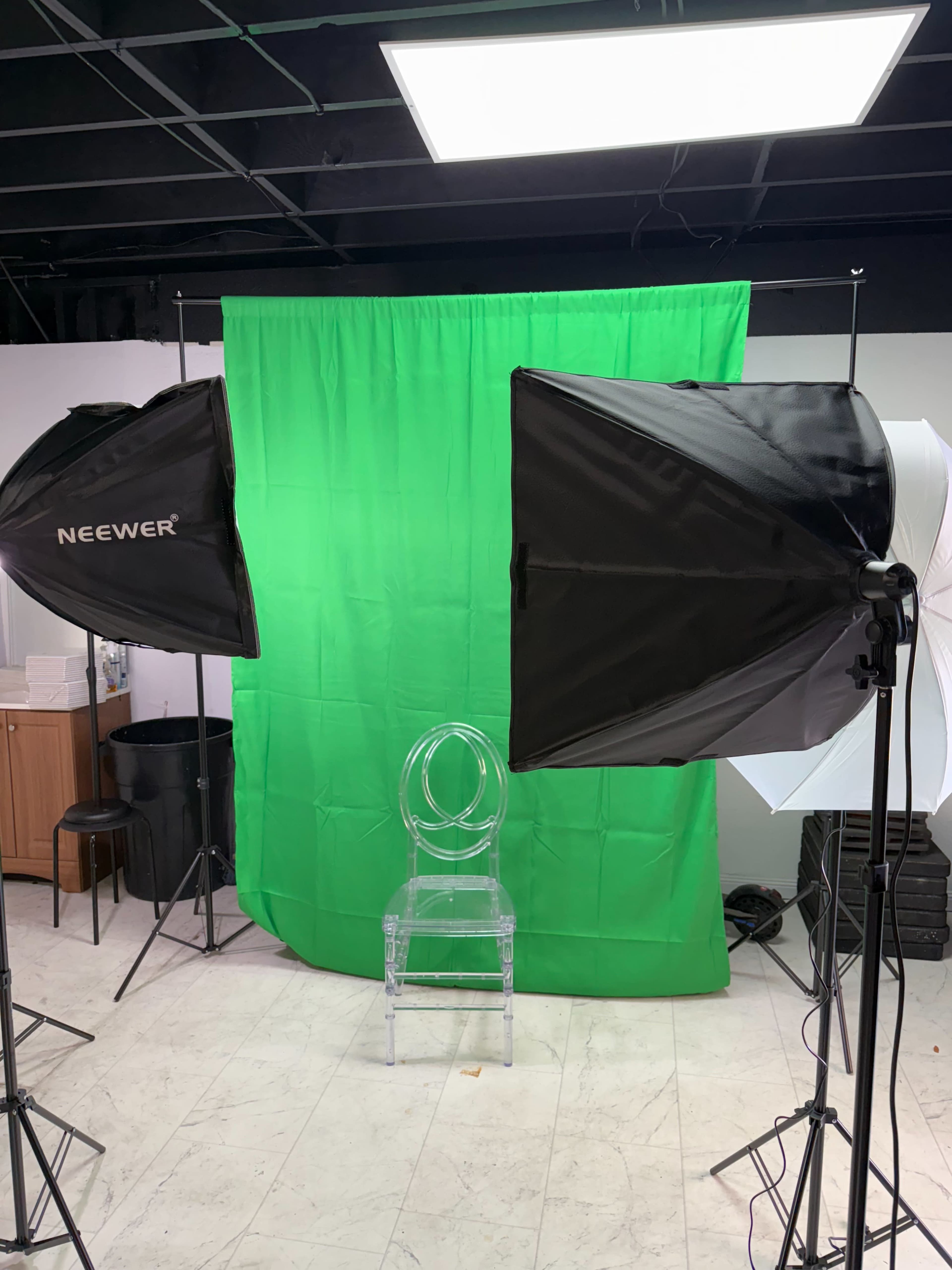 The image shows a photography setup with two softbox lights and a clear acrylic chair positioned in front of a green backdrop.