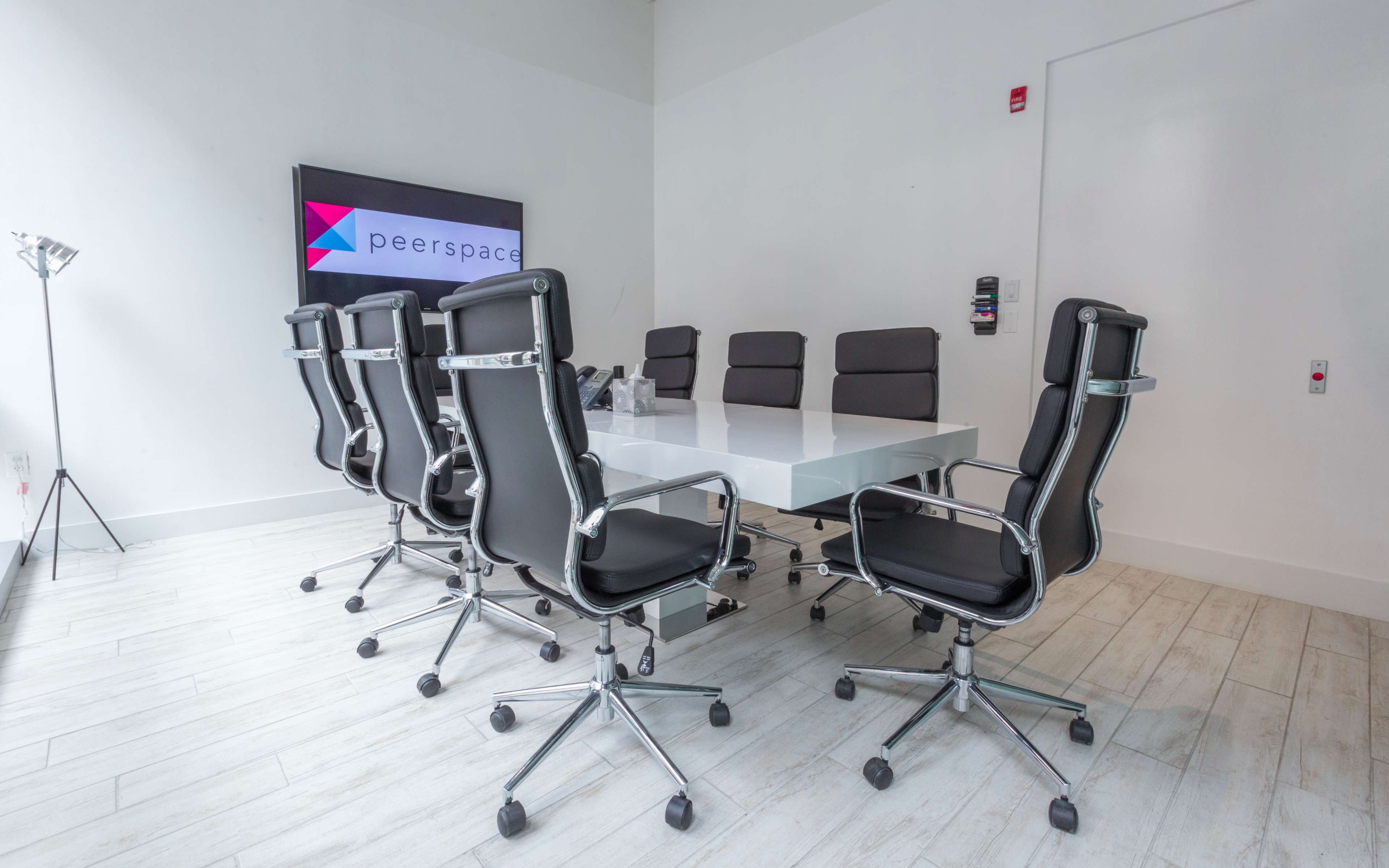 A modern conference room features a long white table surrounded by black chairs and a large screen displaying the Peerspace logo.