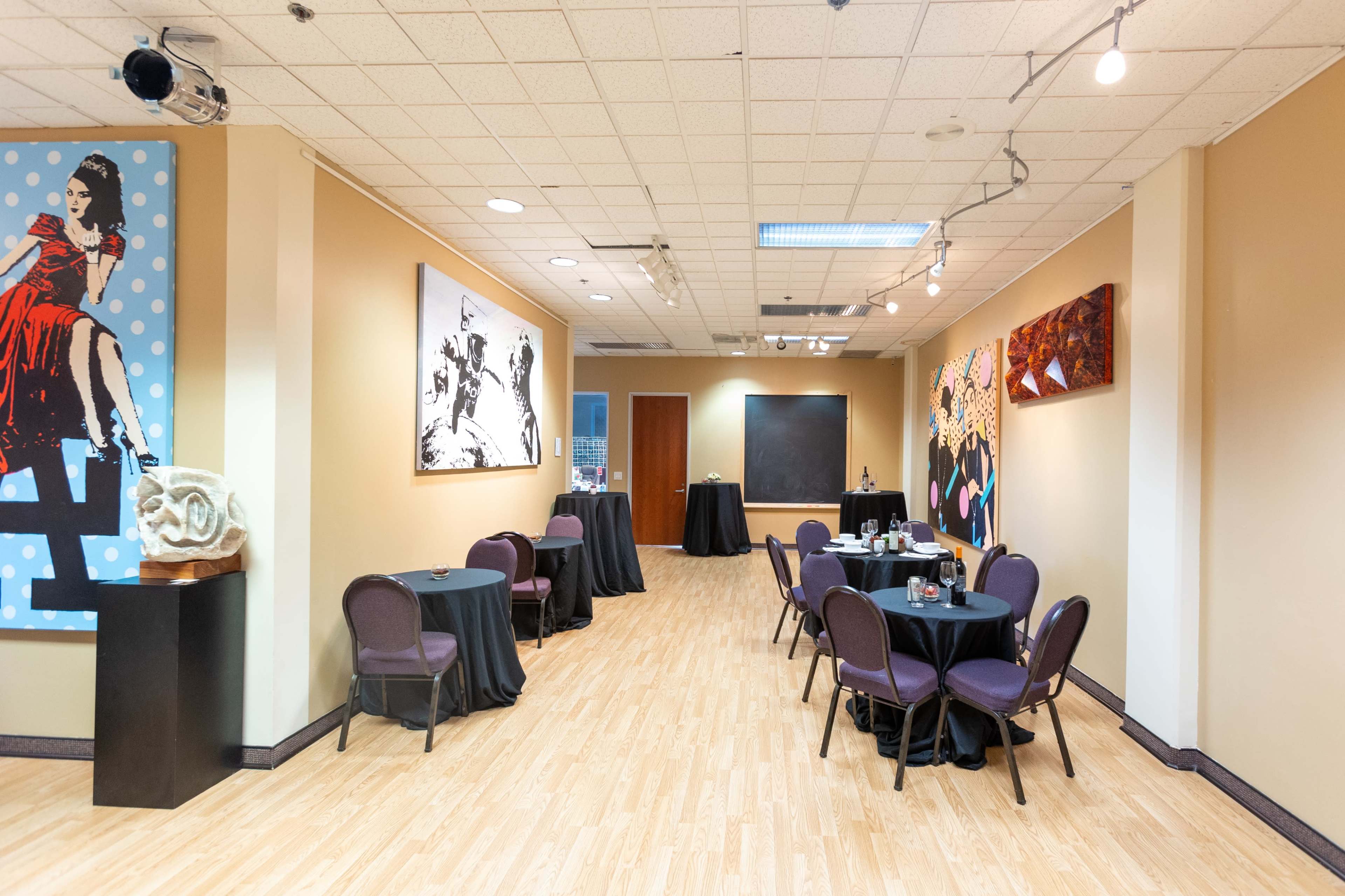 The scene features a spacious room with several round tables covered in black cloth, adorned with artworks on the walls, and minimal decorative elements.