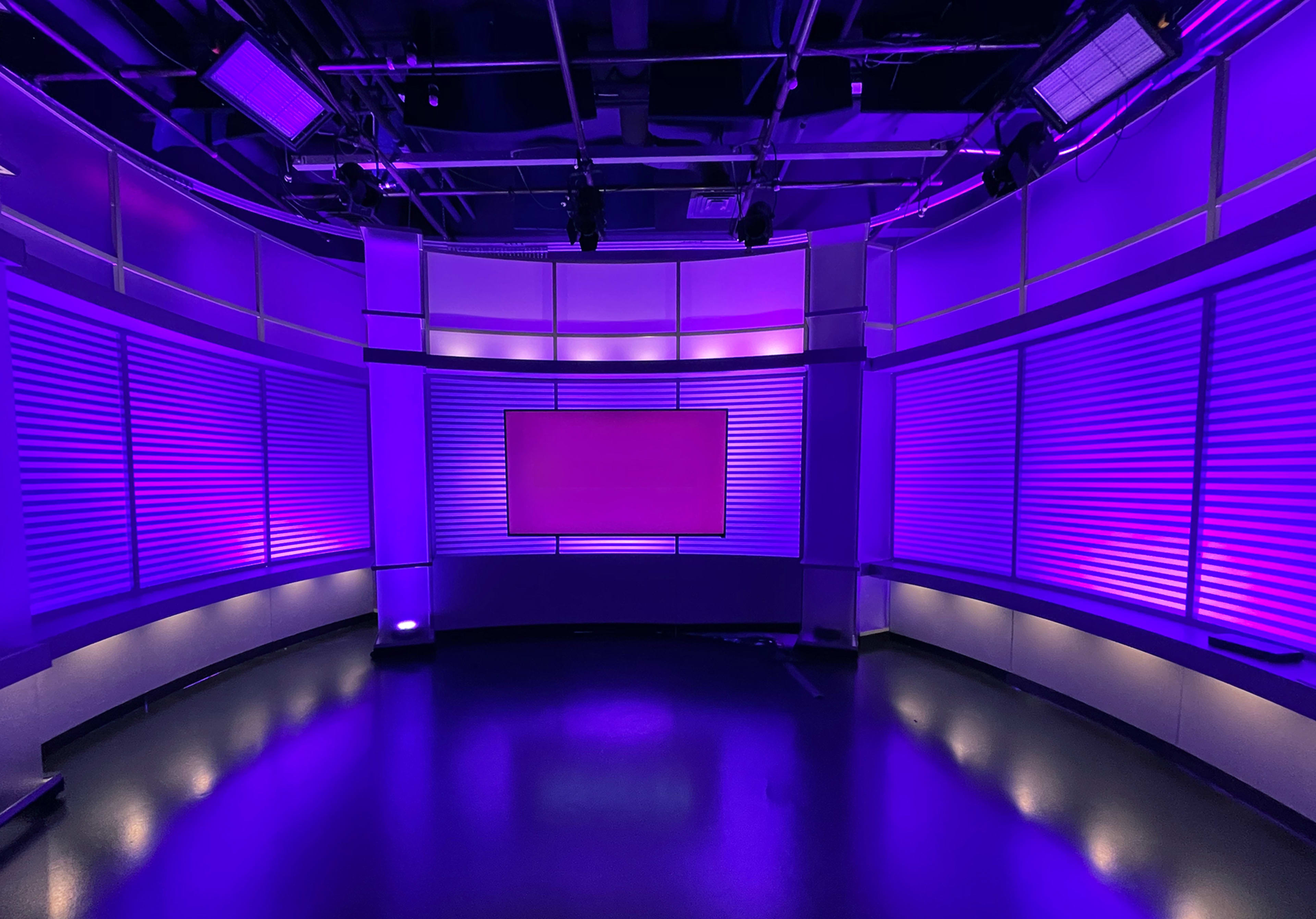 The image shows a modern studio setup with purple lighting and a large empty screen at the center of a curved backdrop.