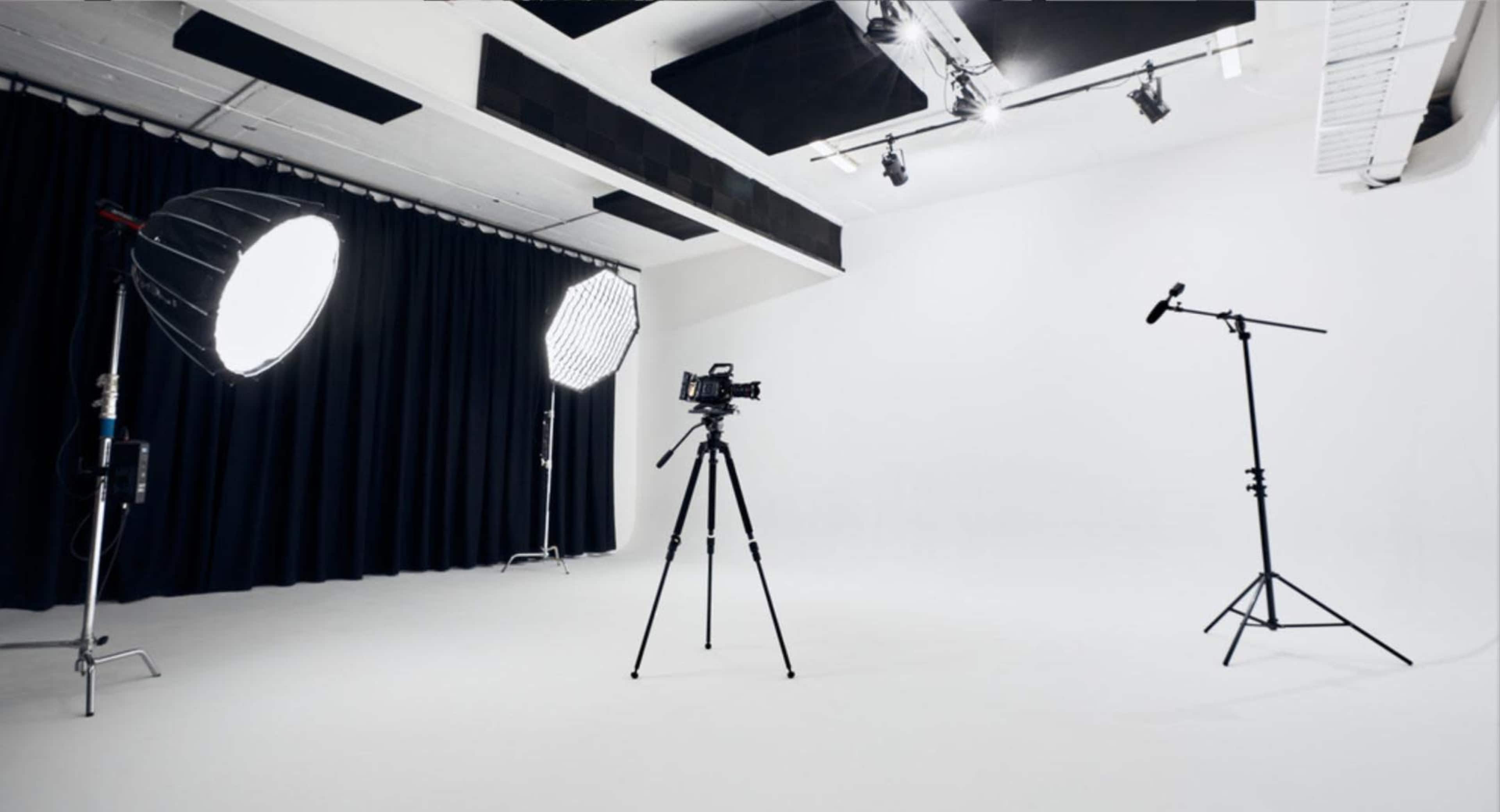 A photography studio equipped with lighting setups, a camera on a tripod, and a microphone on a stand against a plain white background.
