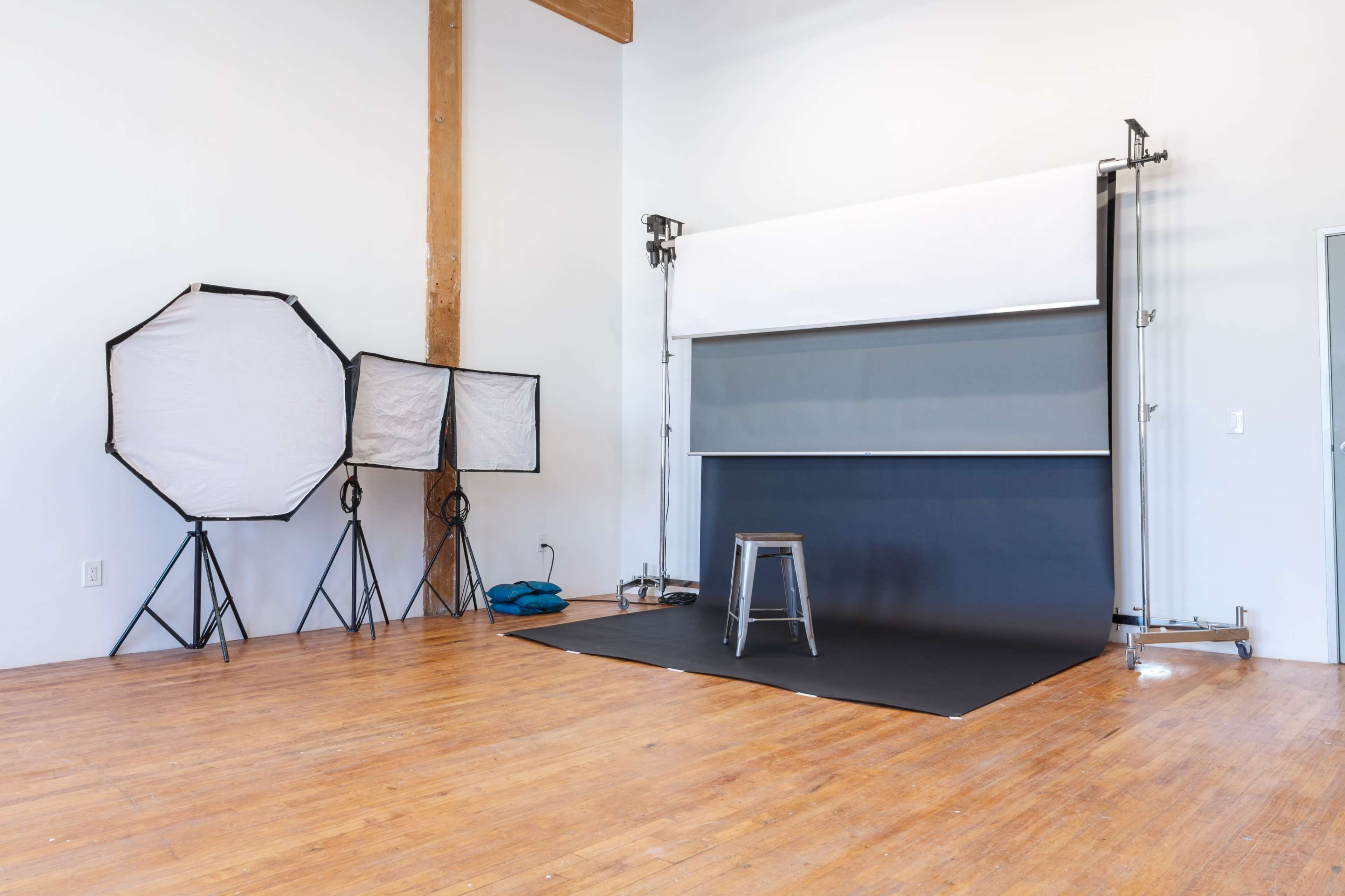 A photography studio with two softboxes, a grey backdrop, a metal stool, and wooden flooring.