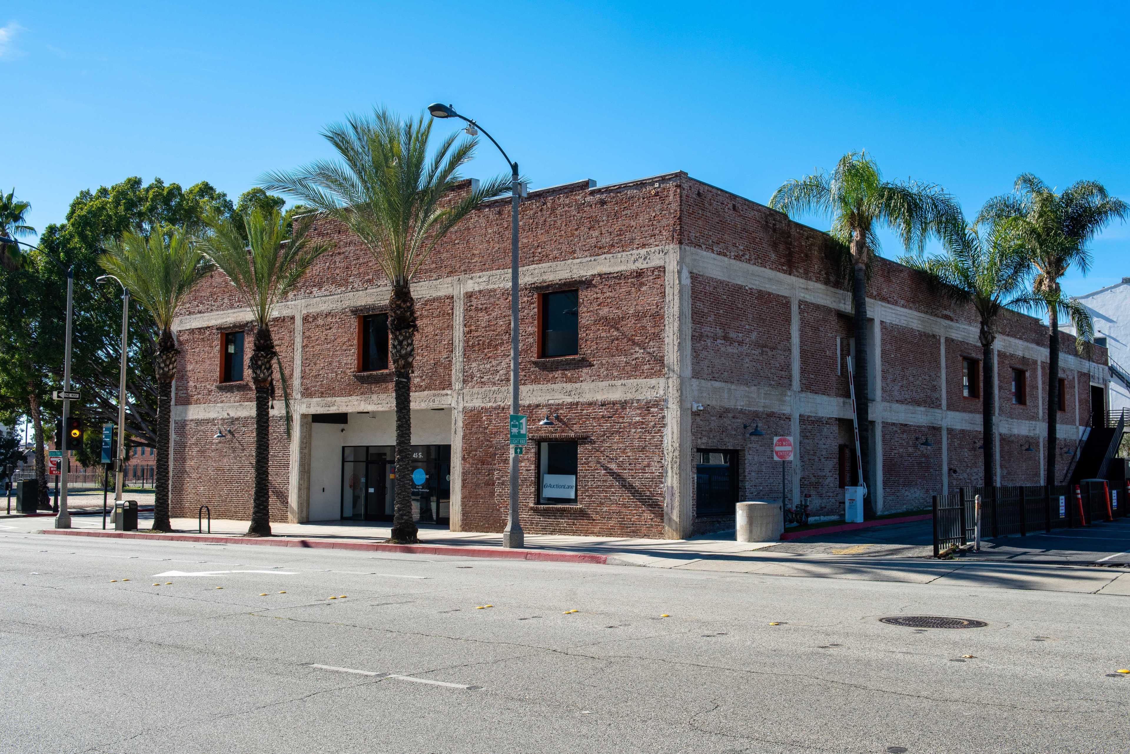 A two-story brick building with palm trees in front, located on a street with clear blue skies.